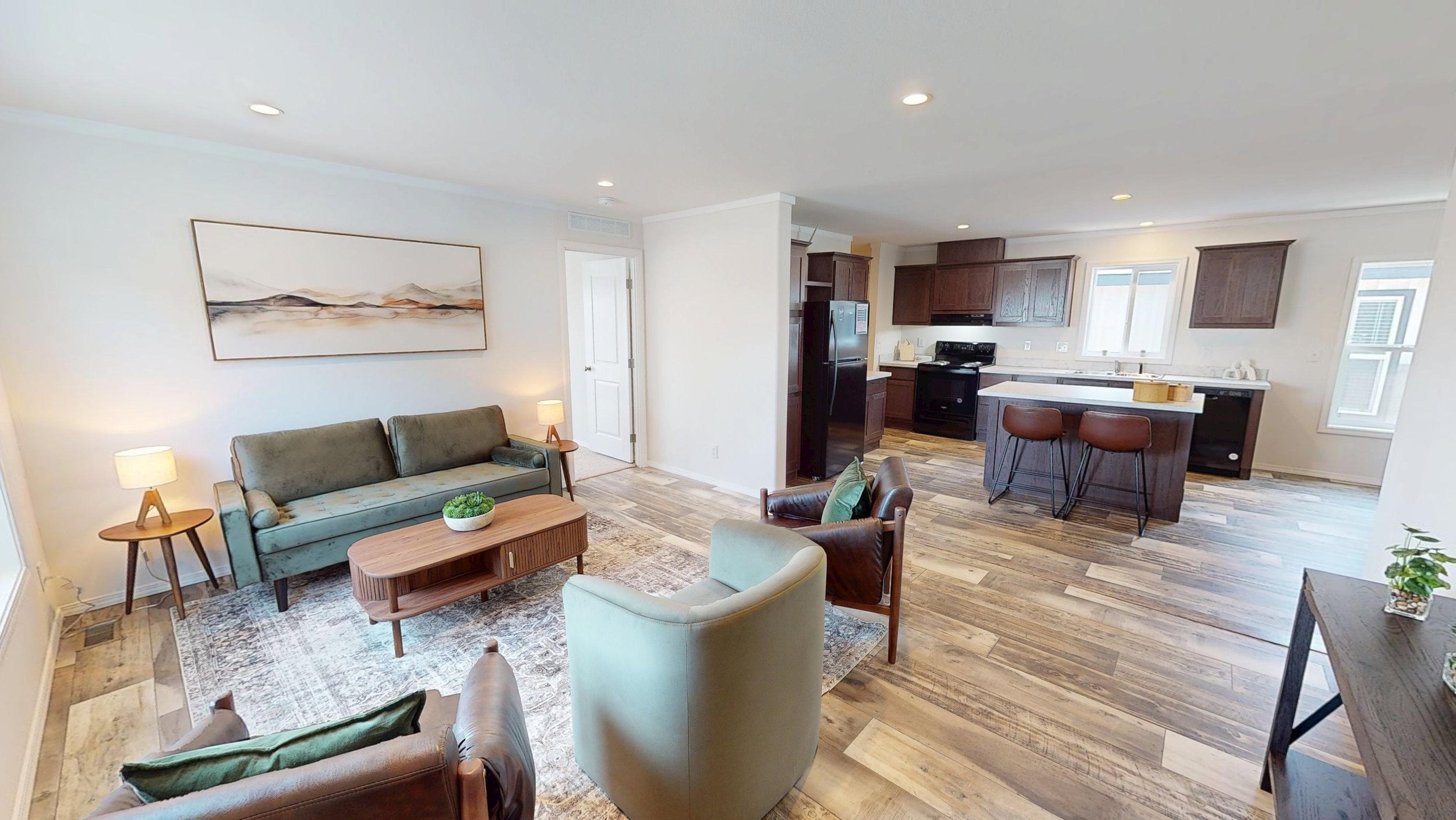Open-concept living room and kitchen with wooden flooring, modern furniture, and white walls.