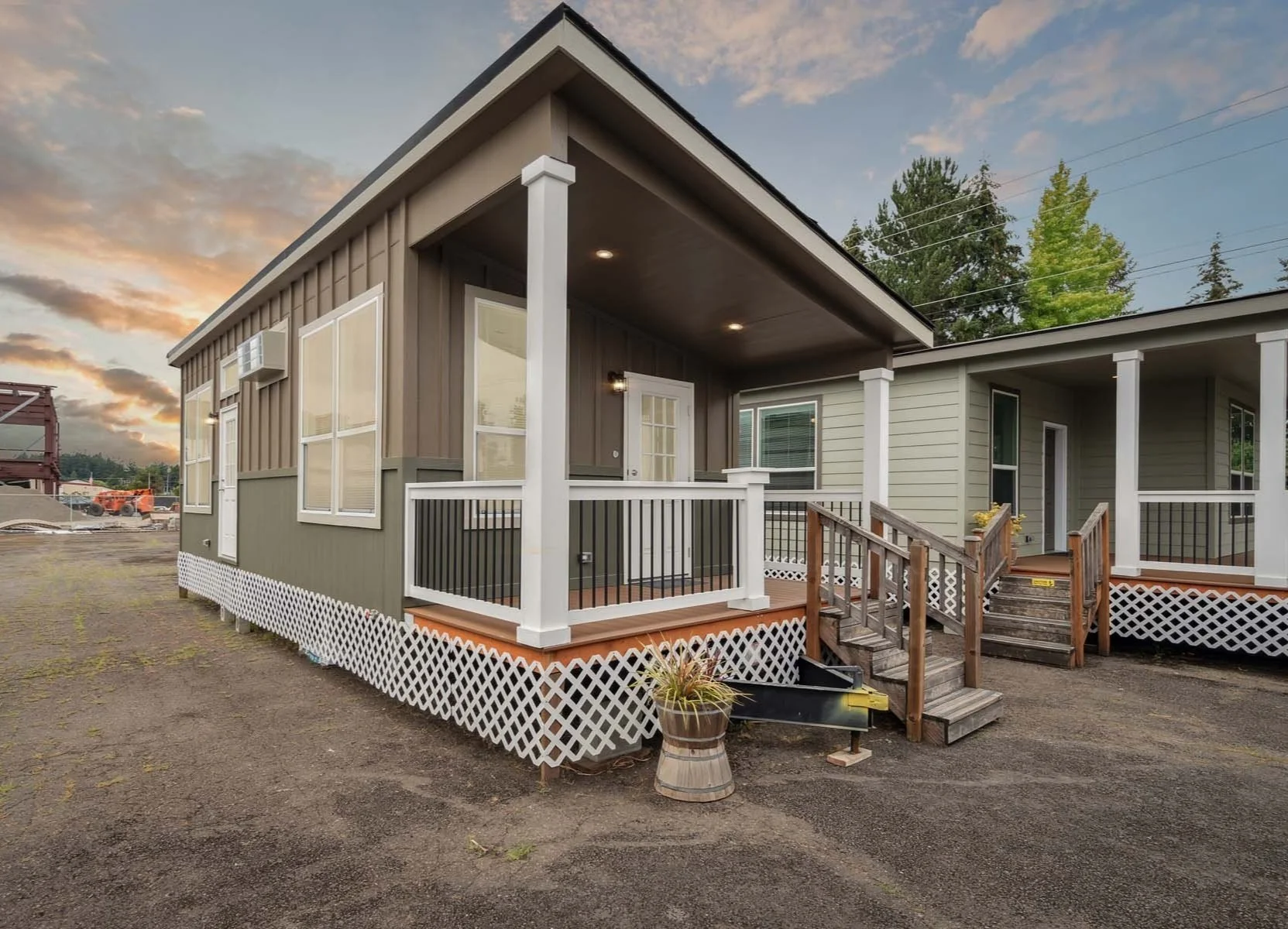 Exterior of a new house with a small porch, white railings, and wooden steps, set on a gravel lot during sunset.