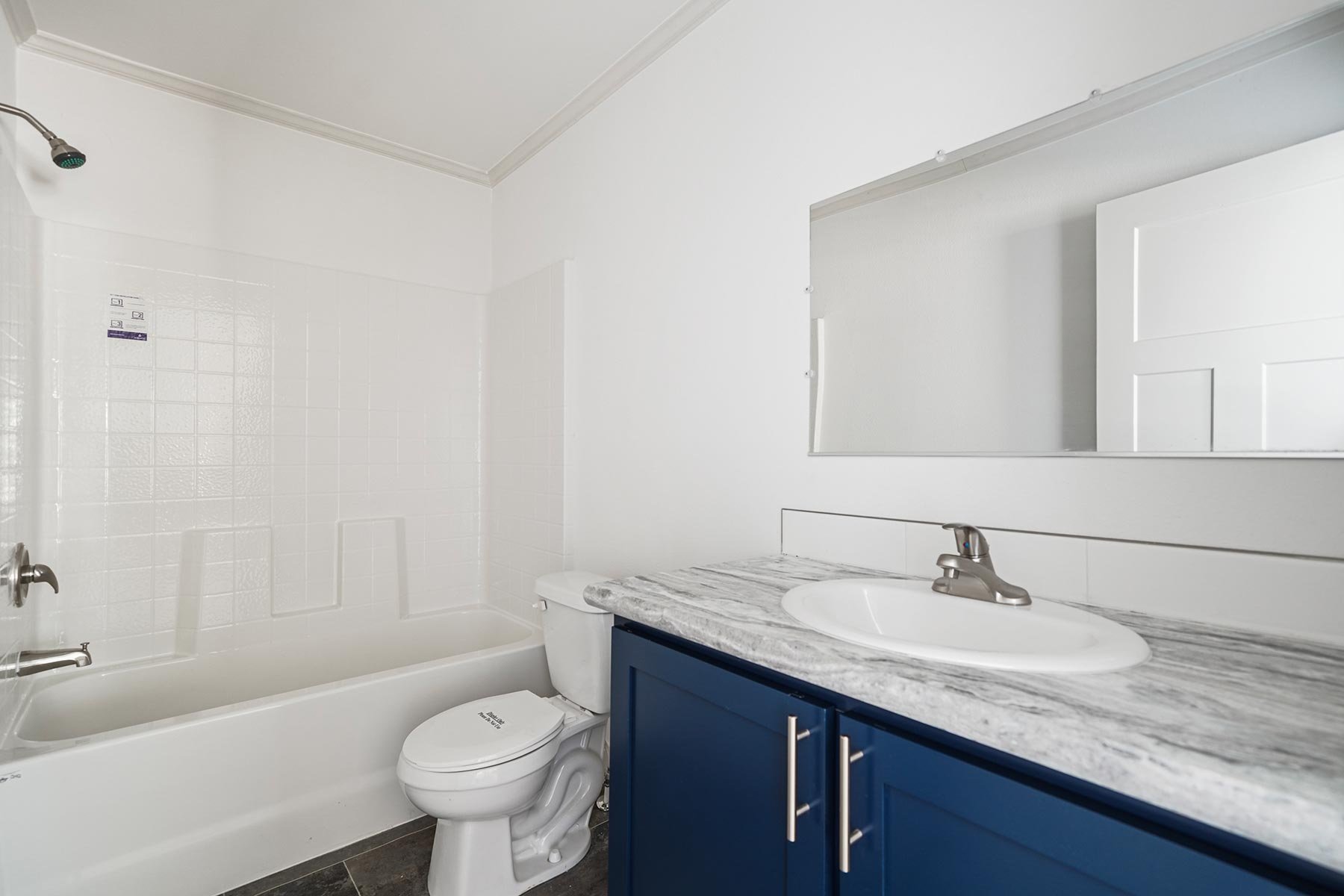 Bathroom with a bathtub, toilet, and blue vanity with a marble countertop and oval sink, large mirror on wall.