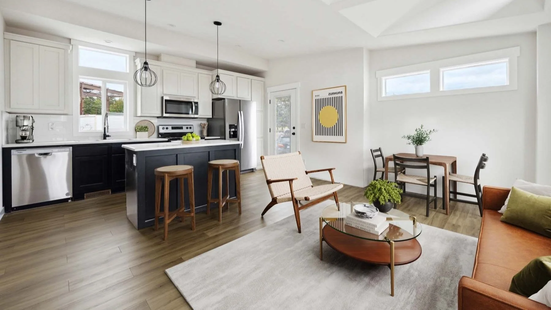 Open concept living room and kitchen with white cabinetry, stainless steel appliances, black island with wooden barstools, and seating area with sofa, armchair, and dining table with chairs, natural light, wood flooring, and modern decor.