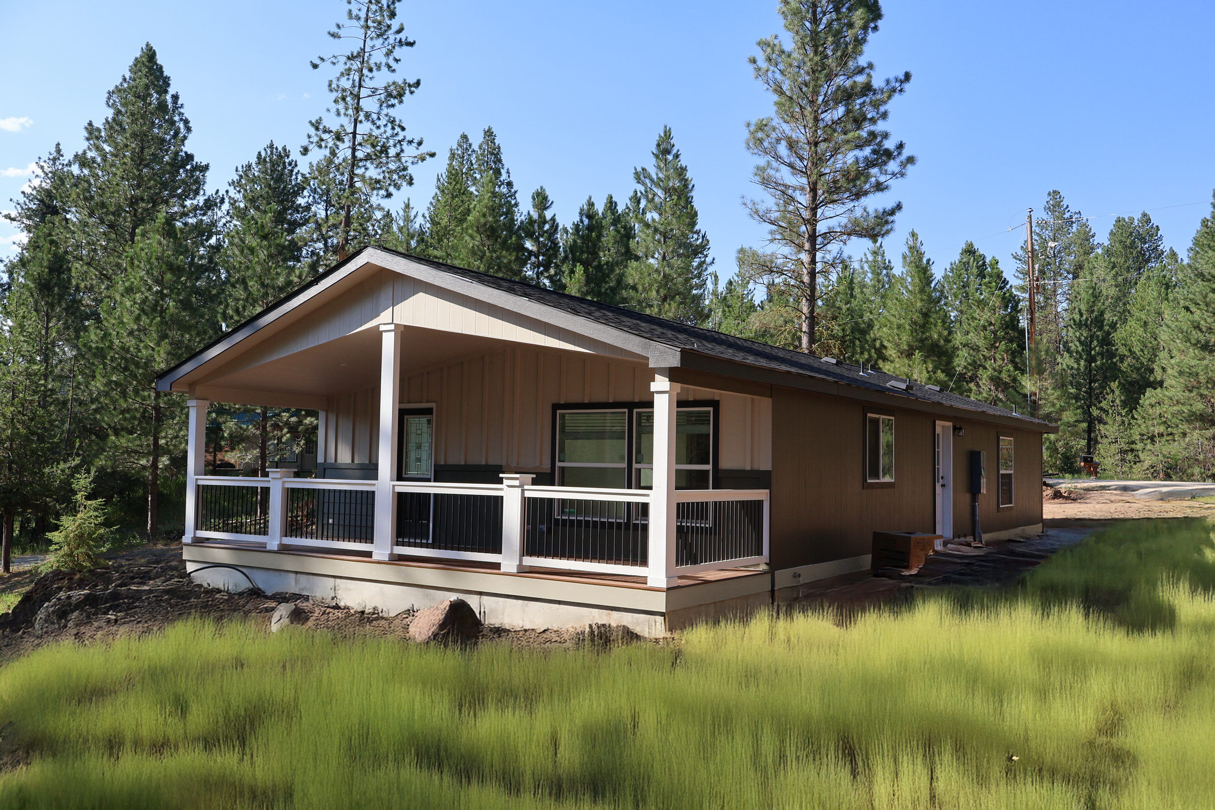 A house with a covered porch, surrounded by trees and grass, under a clear blue sky.