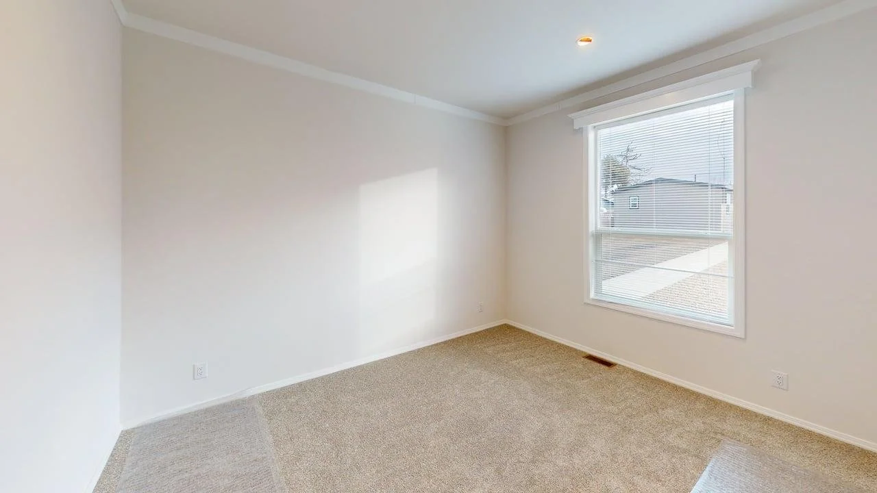 Empty room with white walls, beige carpet, and a large window with blinds letting in natural light.