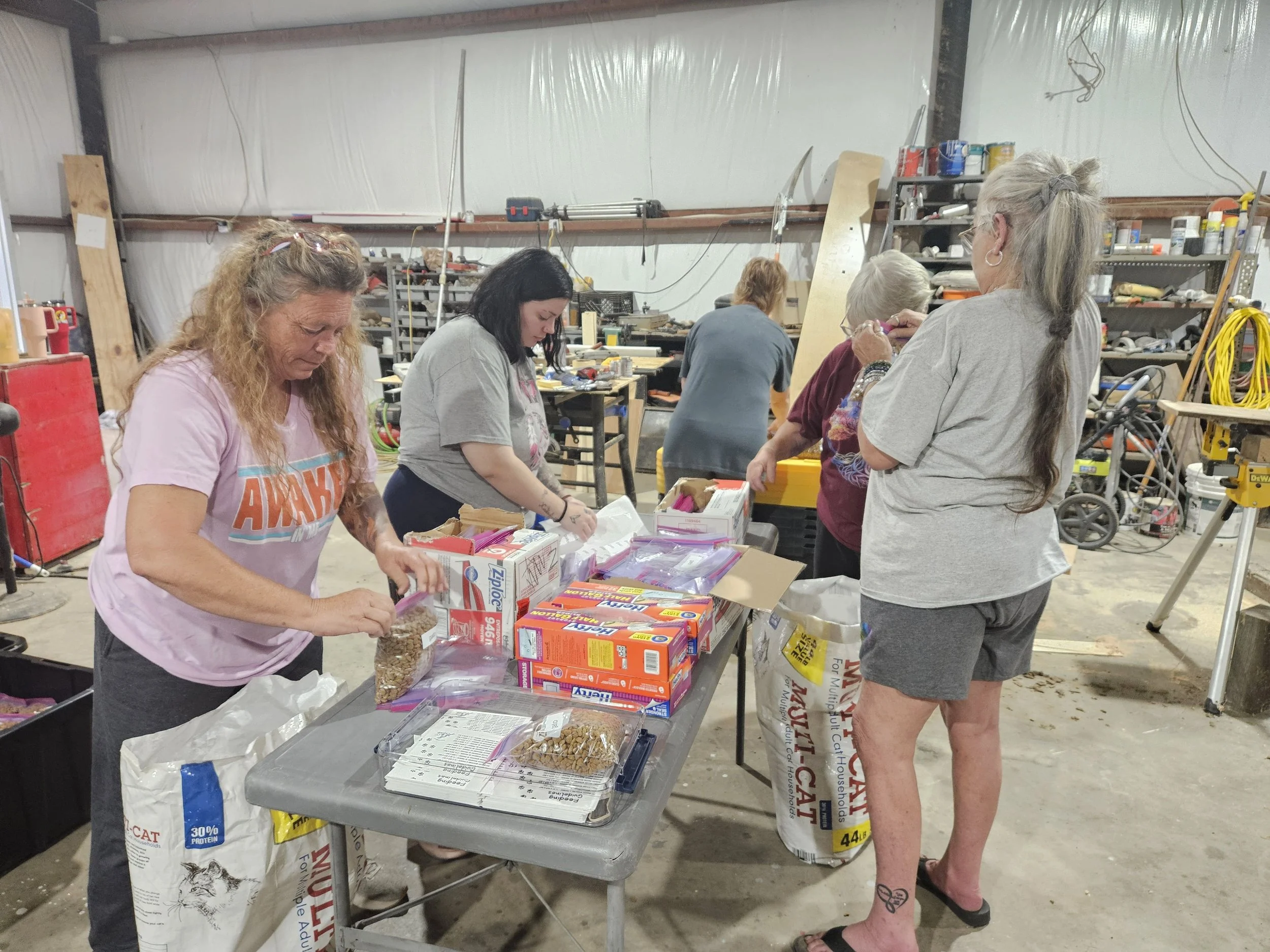 People assembling care packages at a table filled with Ziploc bags and cat food in a workshop.