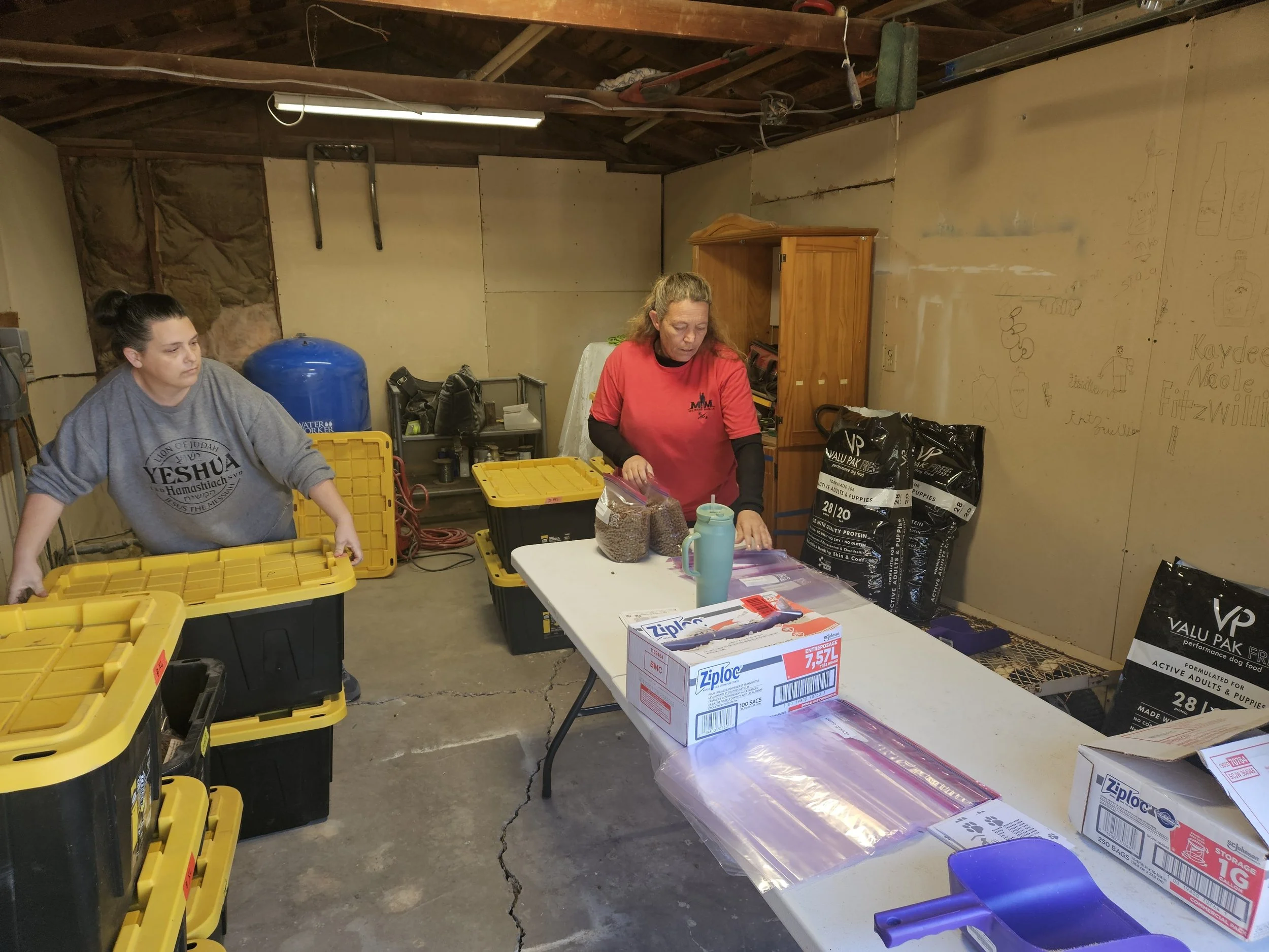 Two people organizing supplies in a garage with storage bins and bags on a table.