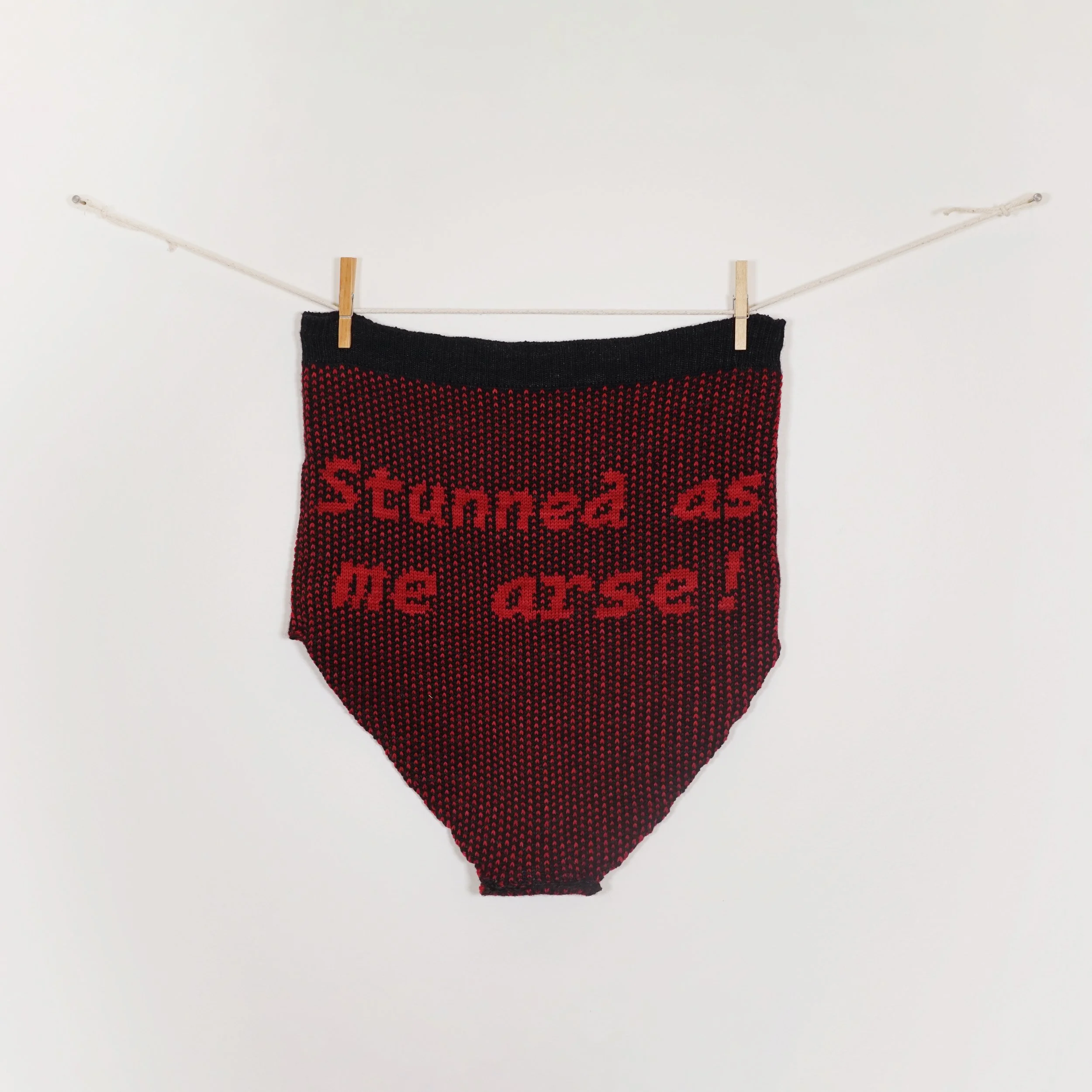 Stunned as me arse, 2026. machine knit merino/nylon wool briefs, cotton cord, wooden clothespins. 44 x 40 cm. Created for Sweetest Little Thing 2026