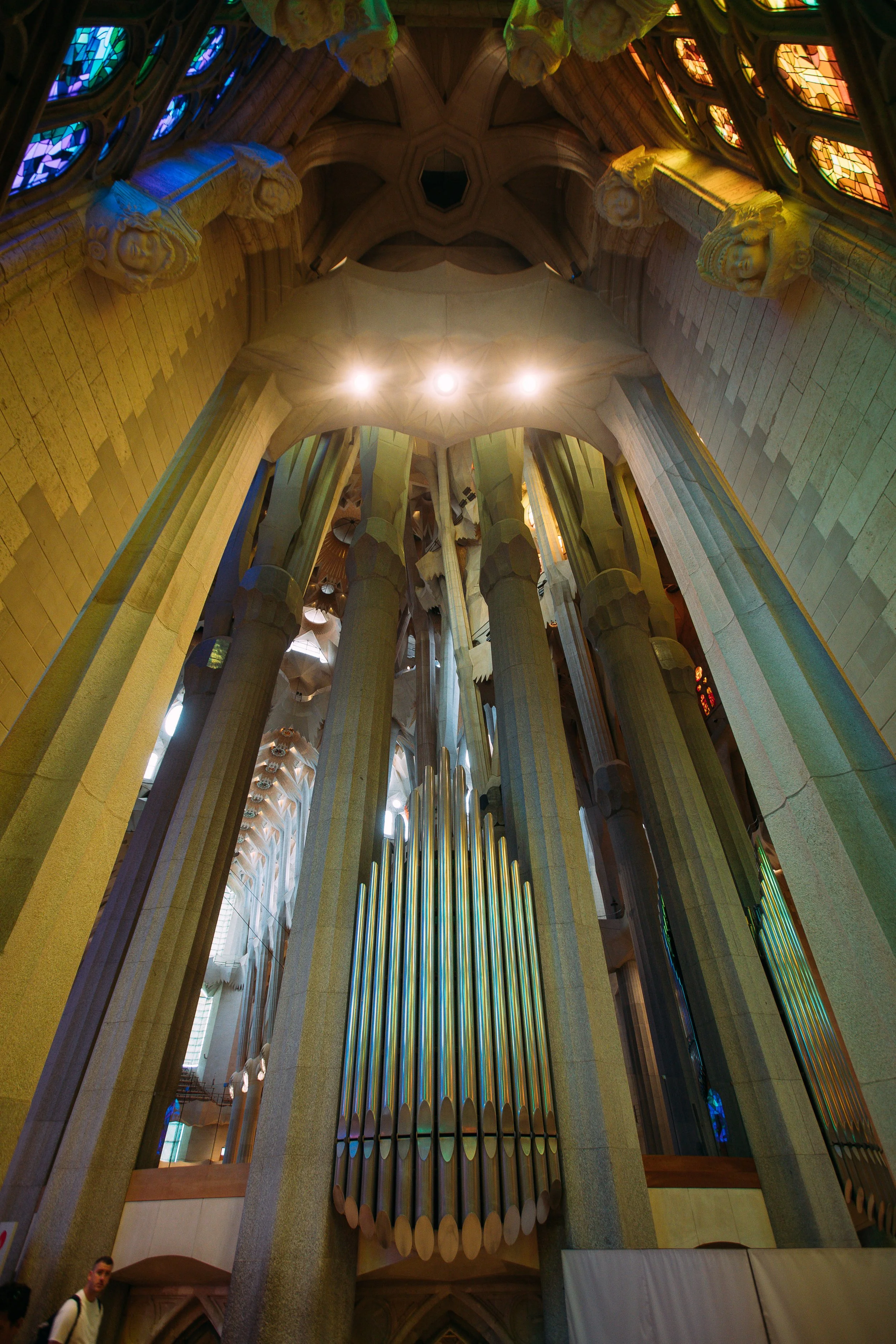Interior view of the Sagrada Familia basilica, showcasing tall columns, stained glass windows, and a large pipe organ with vertical pipes.