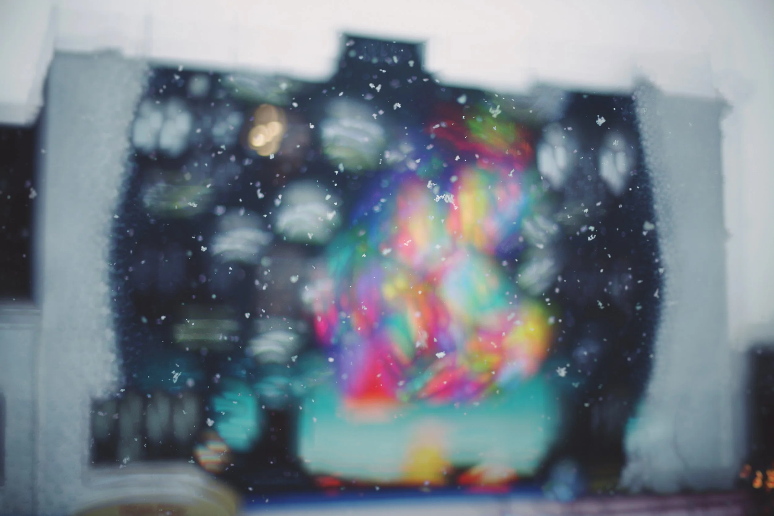 Colorful rainbow light reflection on a dark window with water droplets, slightly out of focus.