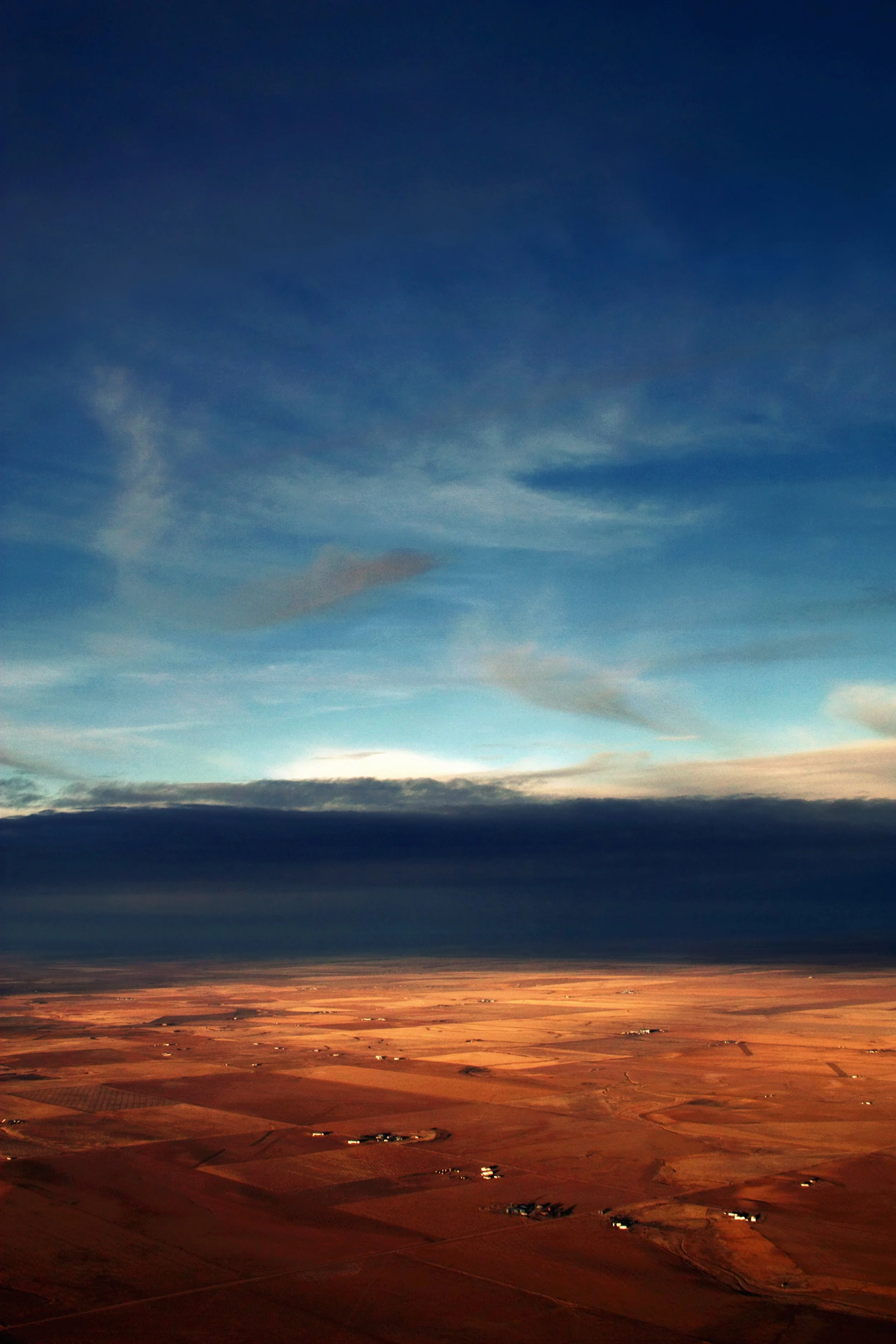 Aerial view of farmland at sunset or sunrise with the sky transitioning from light to dark blue and orange on the horizon.