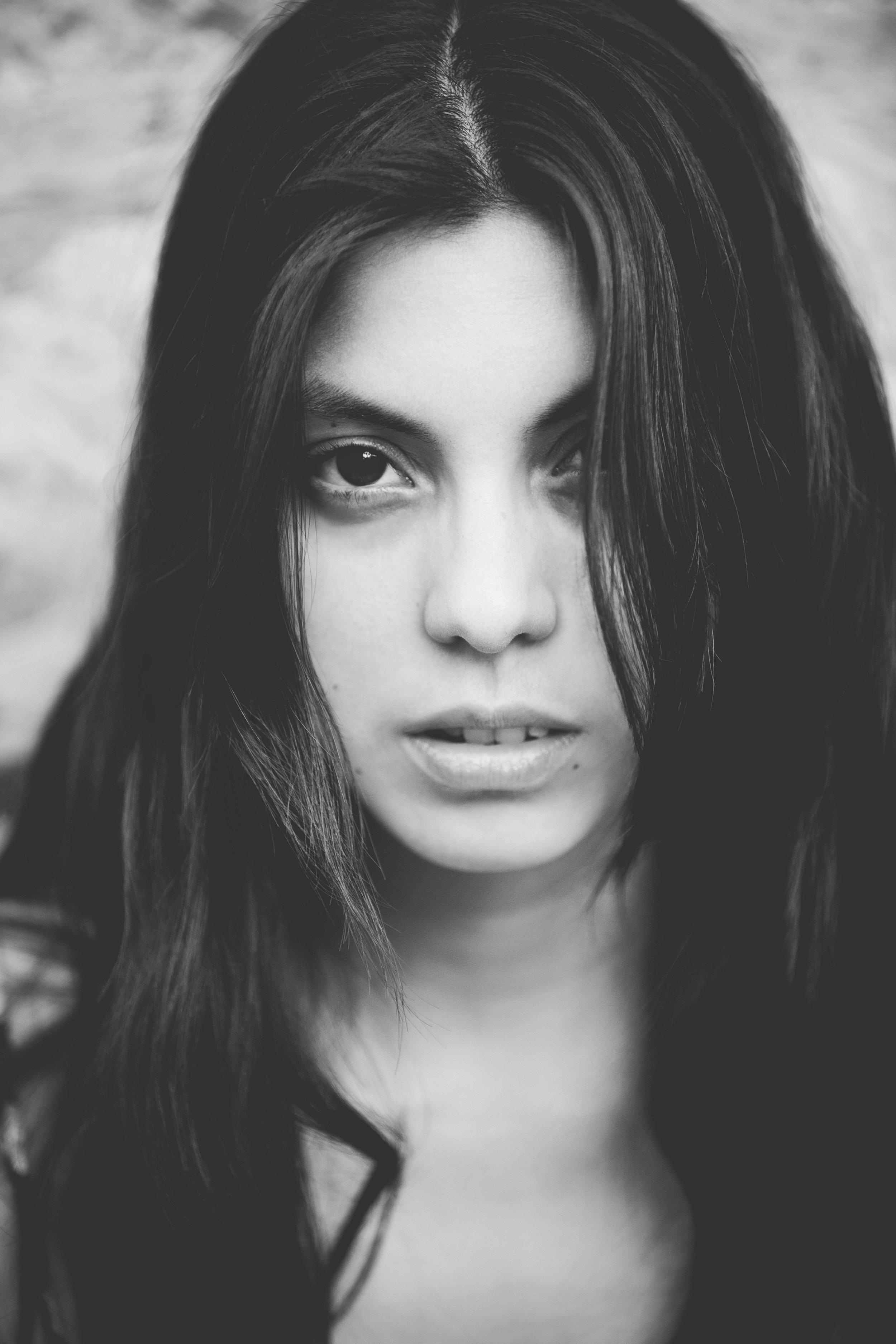 Black and white close-up of a woman's face with long hair, partially covering one eye, with a blurred background.