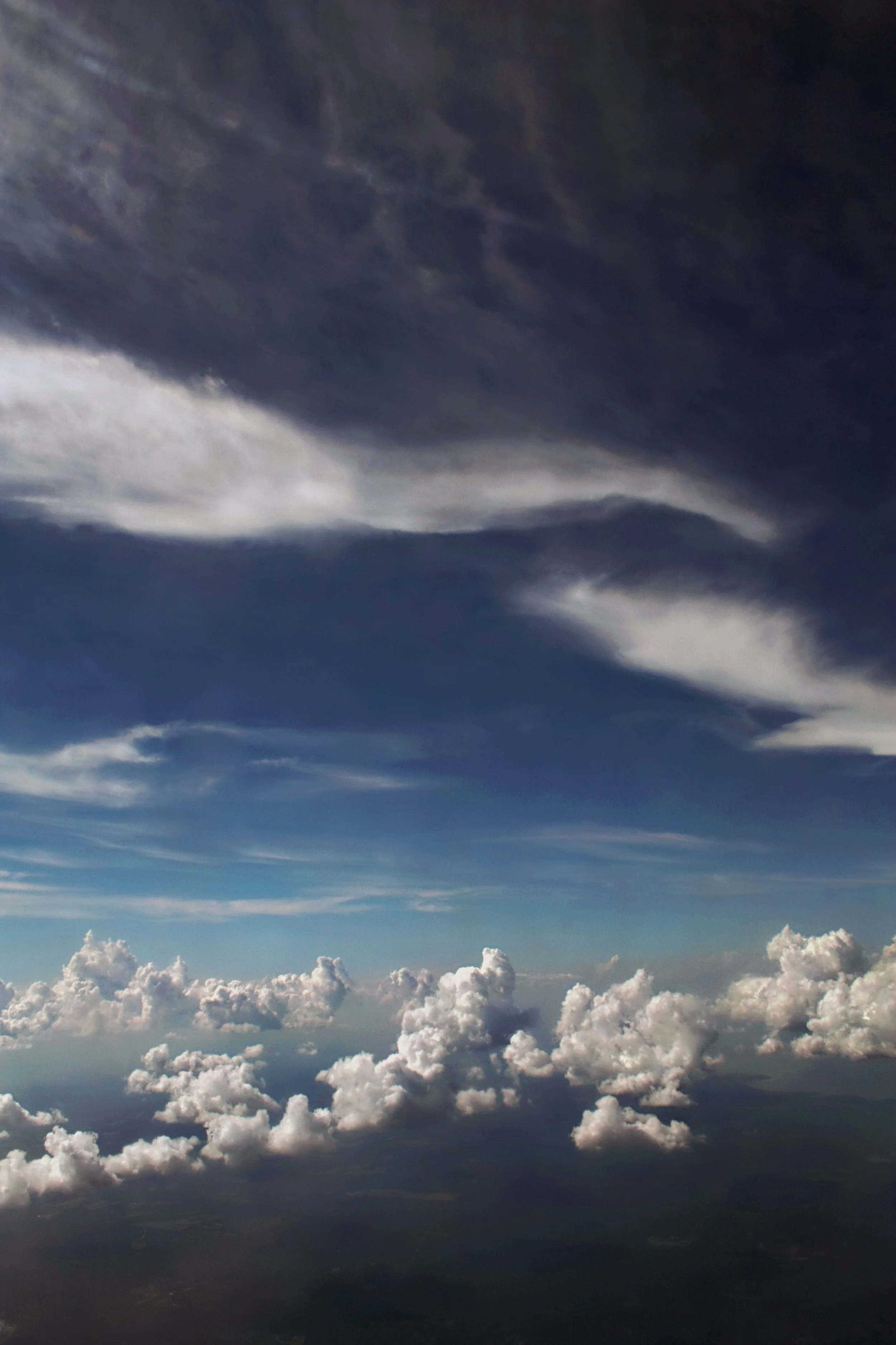 A view of dark storm clouds and lighter fluffy clouds from above, possibly taken from an airplane.