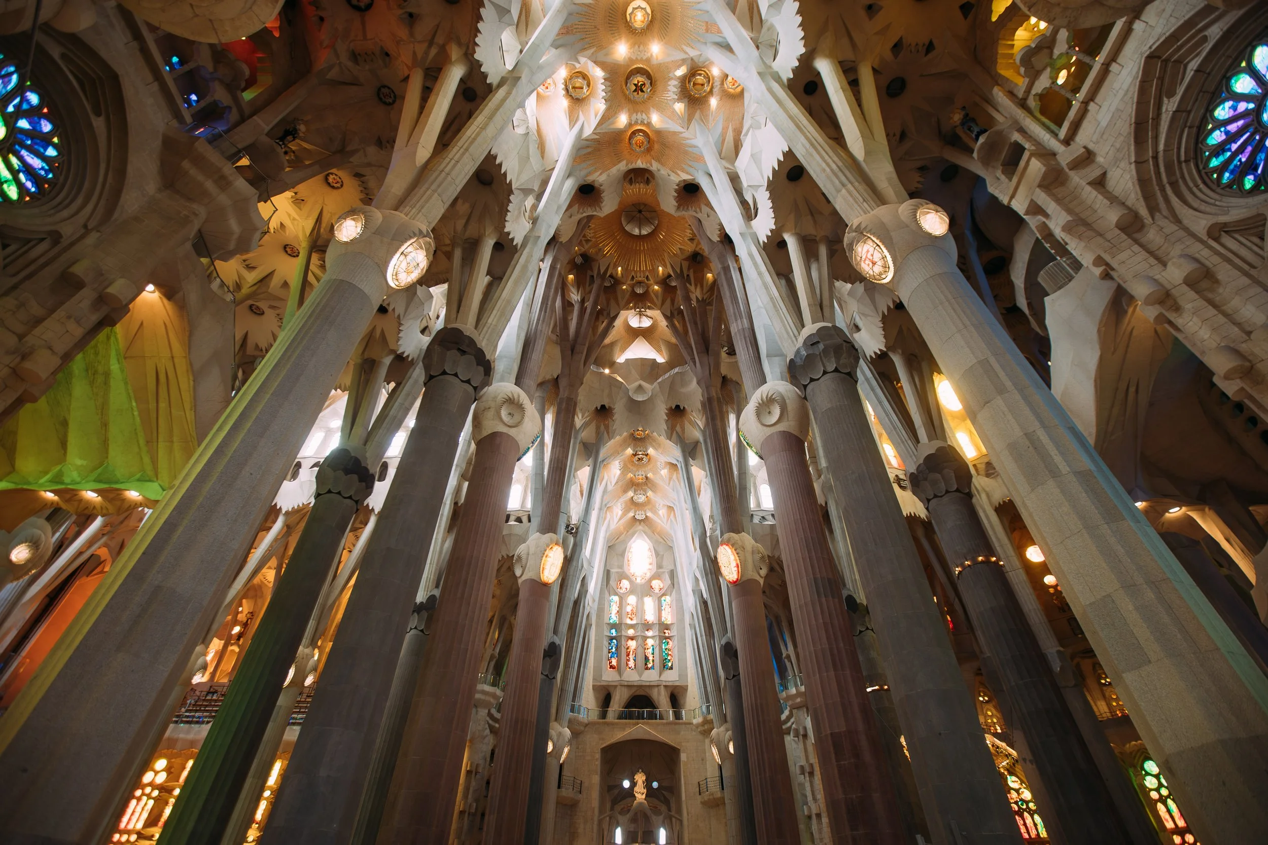 Inside the basilica of Sagrada Familia, showing towering columns and intricate stained glass windows.