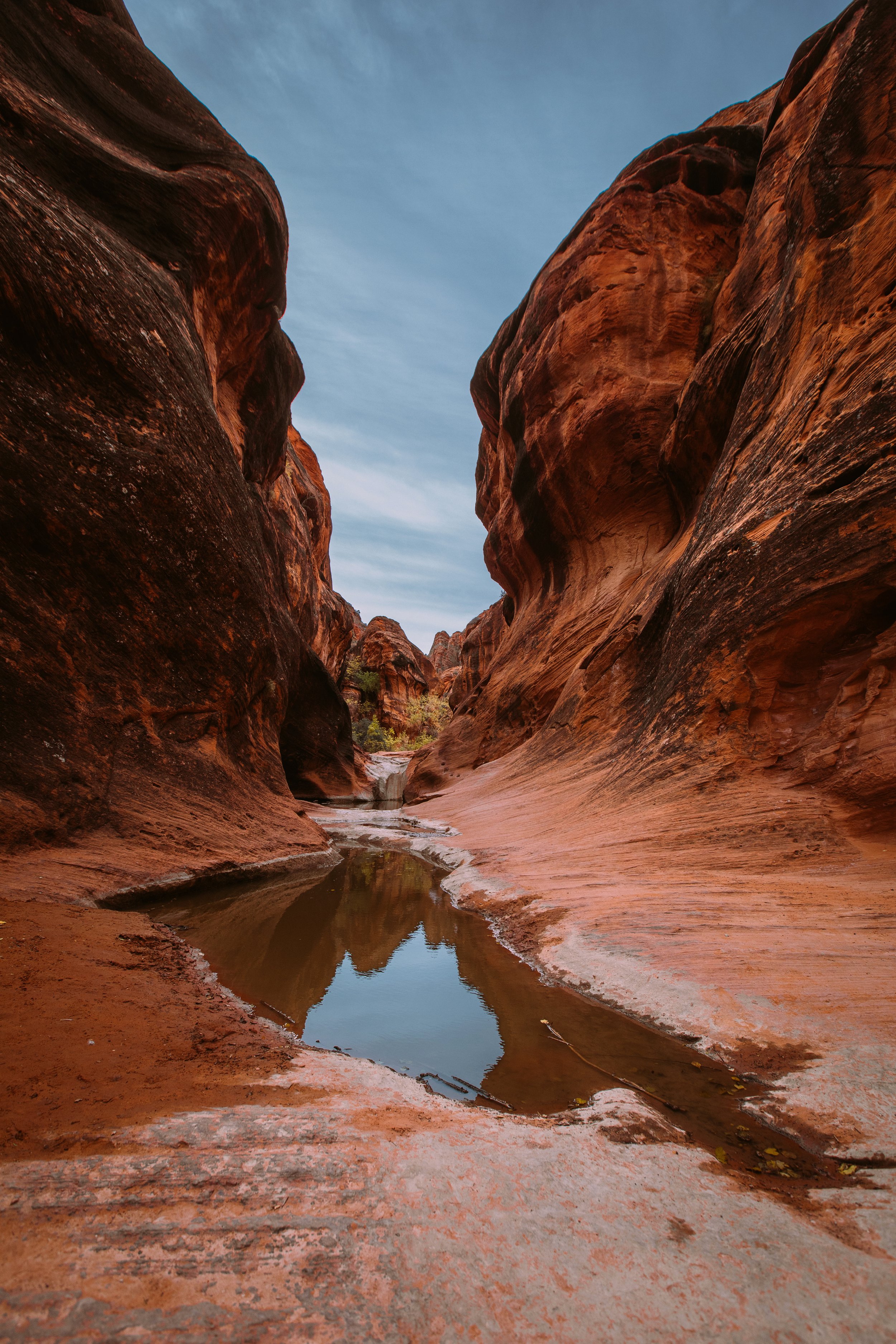 Red sandstone canyon walls with a small pool of water reflecting the sky.