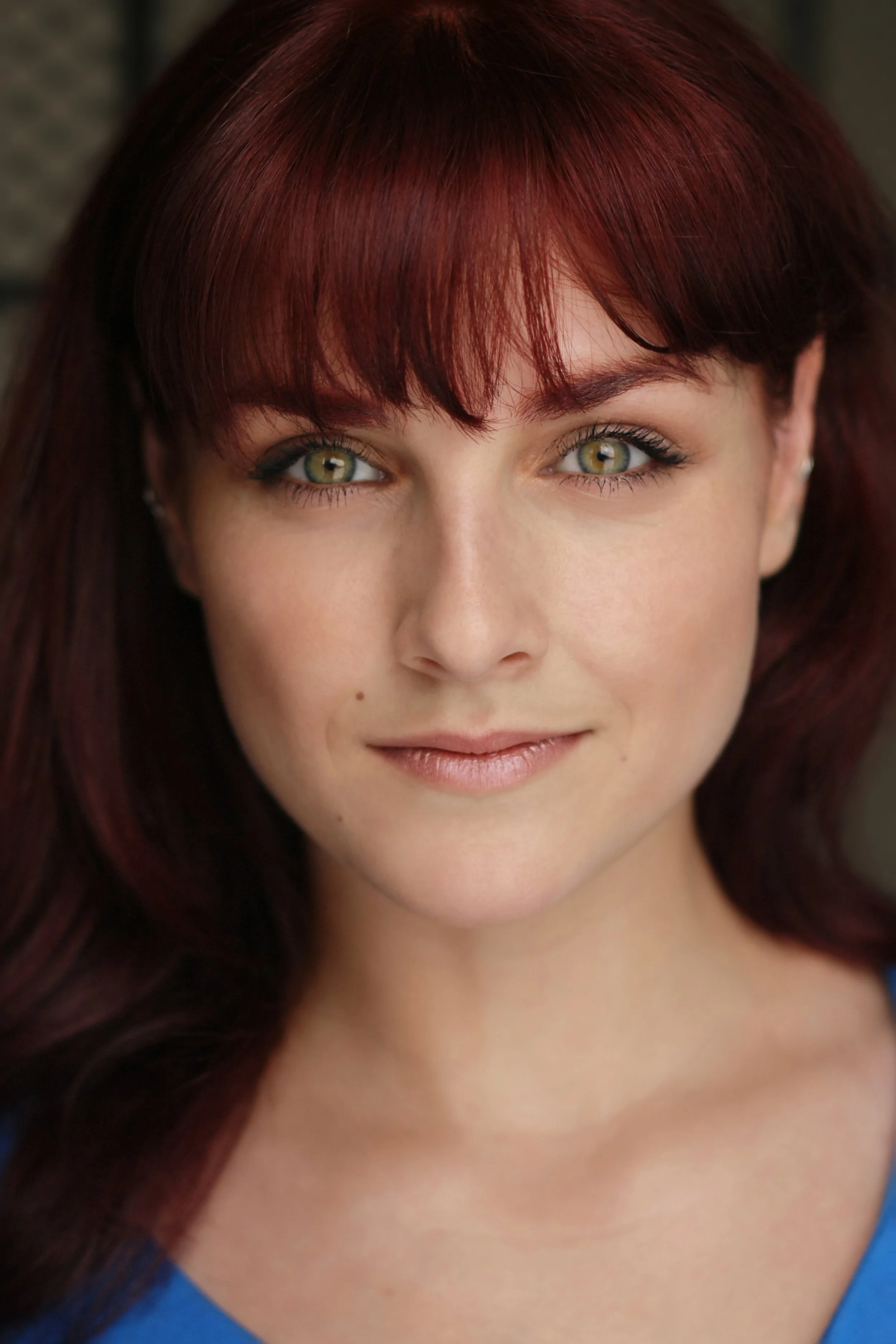 Close-up of a woman with red hair and green eyes, wearing a blue top, smiling softly.