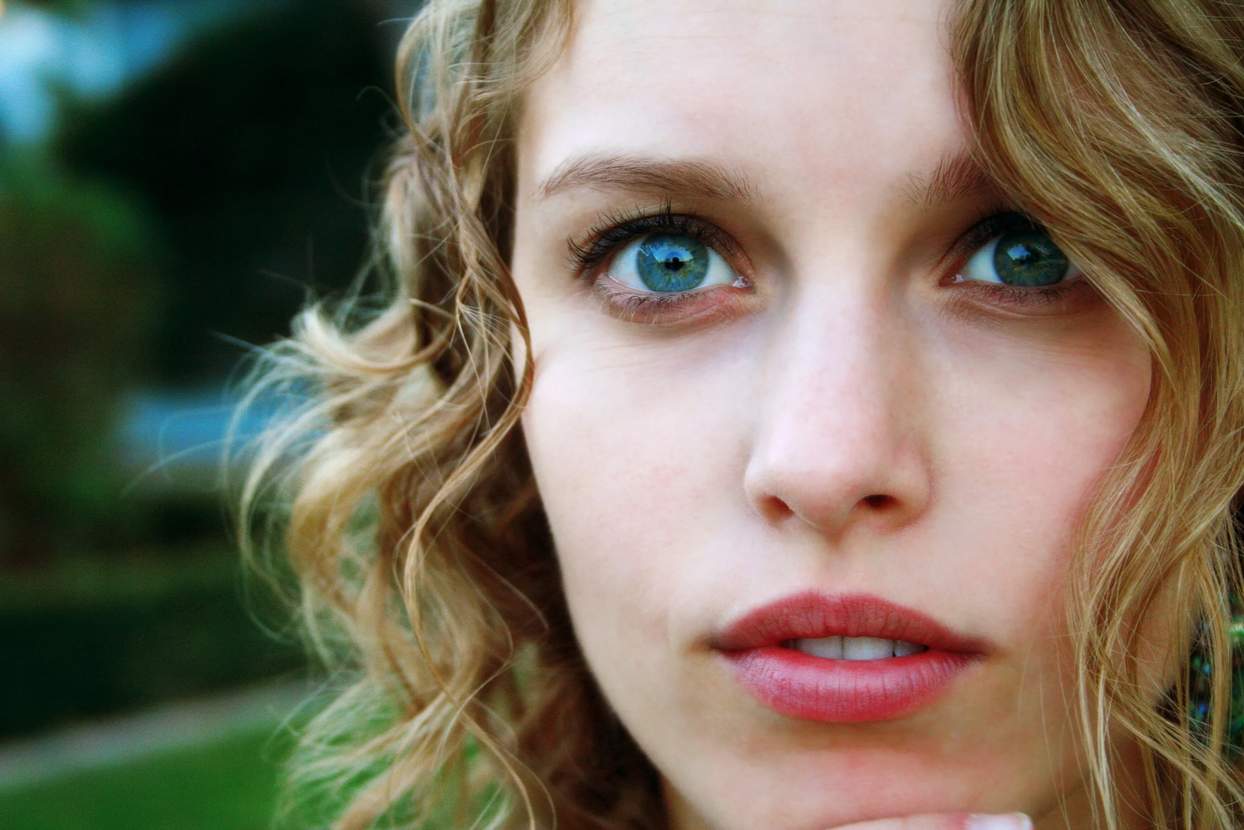 Close-up of a woman's face focusing on her blue eyes, curly blonde hair, and pink lips.