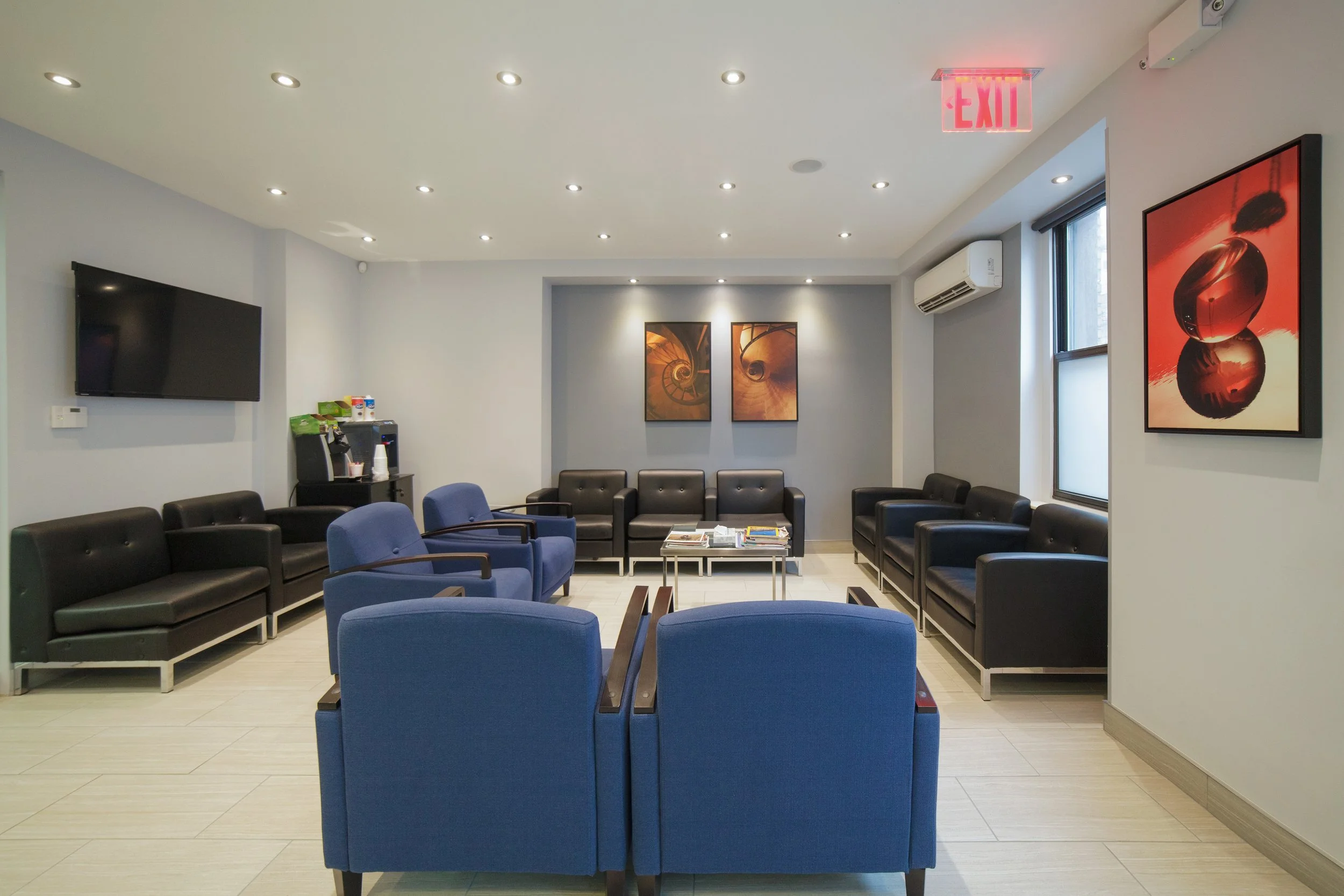 Waiting room with blue and black chairs, wall art, a wall-mounted TV, and a coffee station.