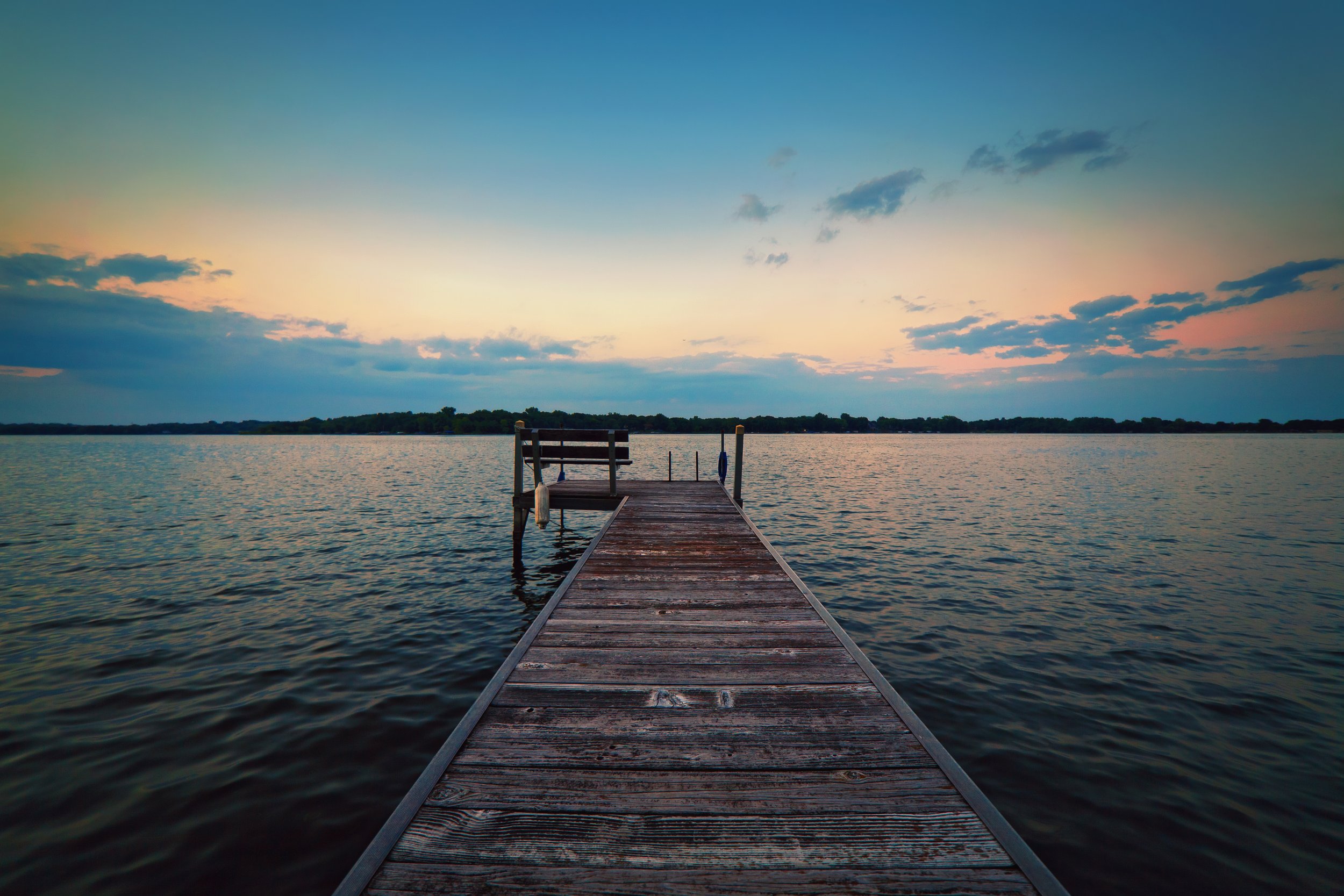 A wooden dock extending into a calm body of water under a colorful sunset sky with scattered clouds.