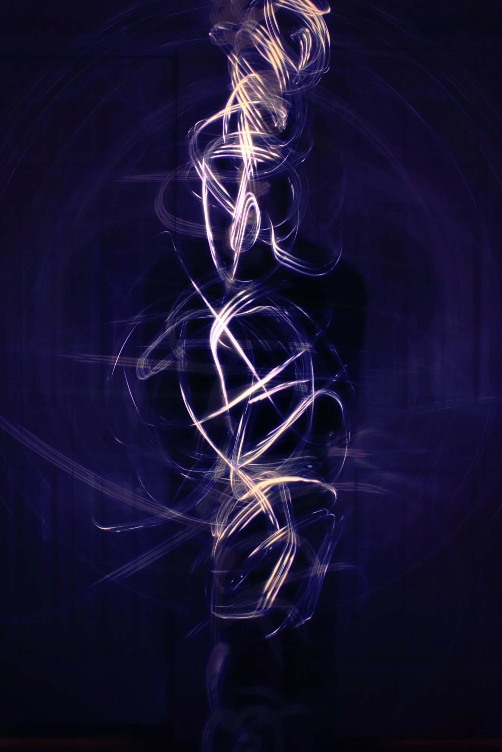 Light trails in purple and yellow hues forming a complex swirling pattern against a dark background.