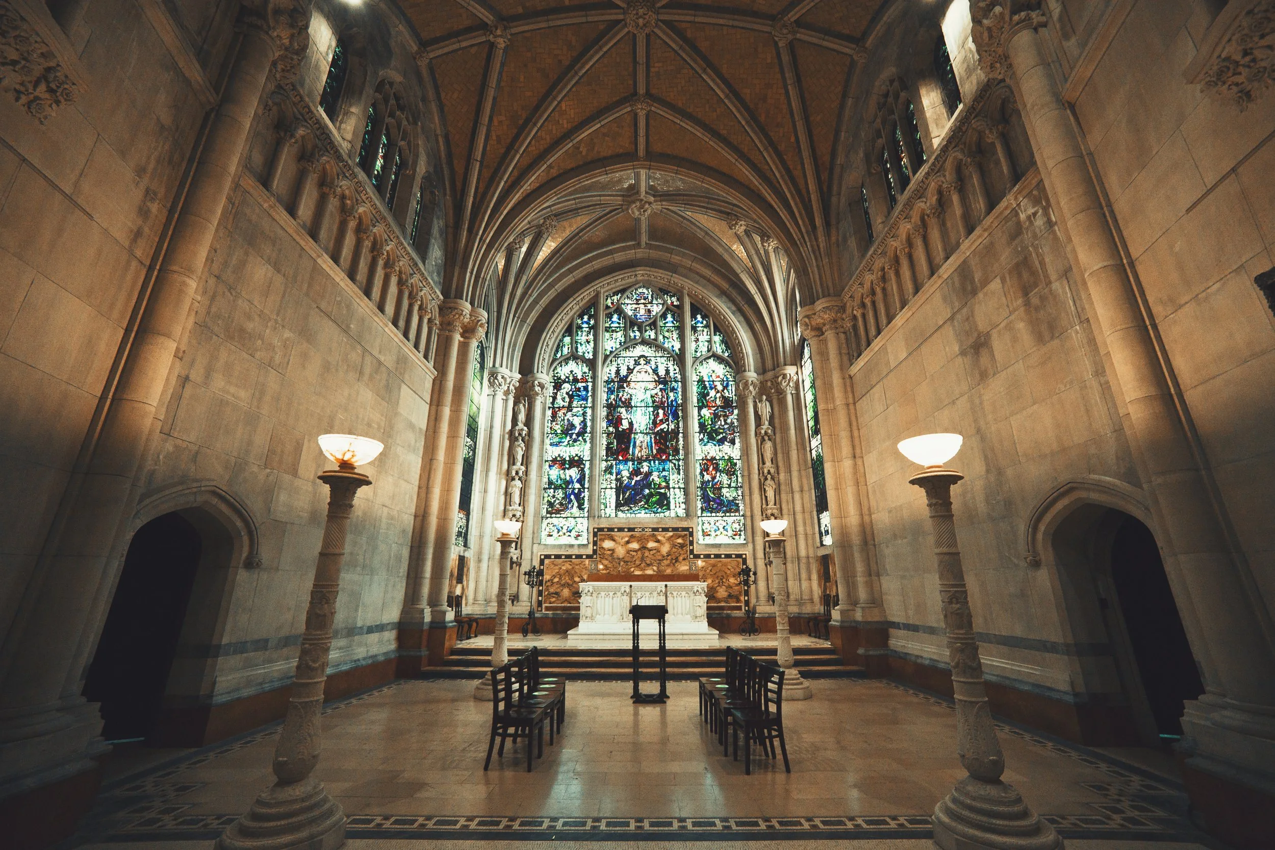 Interior of a historic church or cathedral with high vaulted ceiling, stained glass windows, stone columns, and altar at the front.