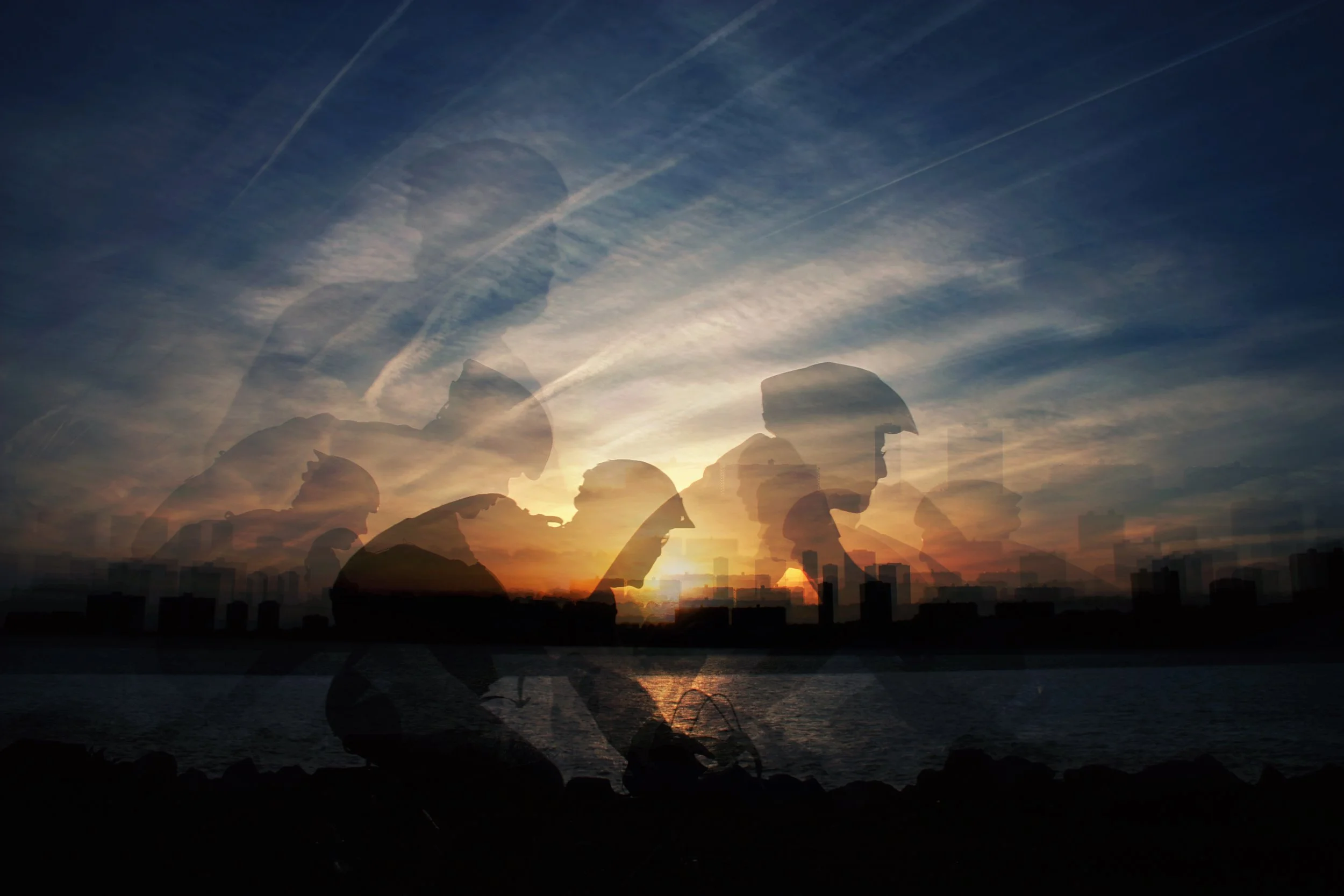 Silhouettes of people wearing safety helmets with a city skyline and ocean in the background at sunset