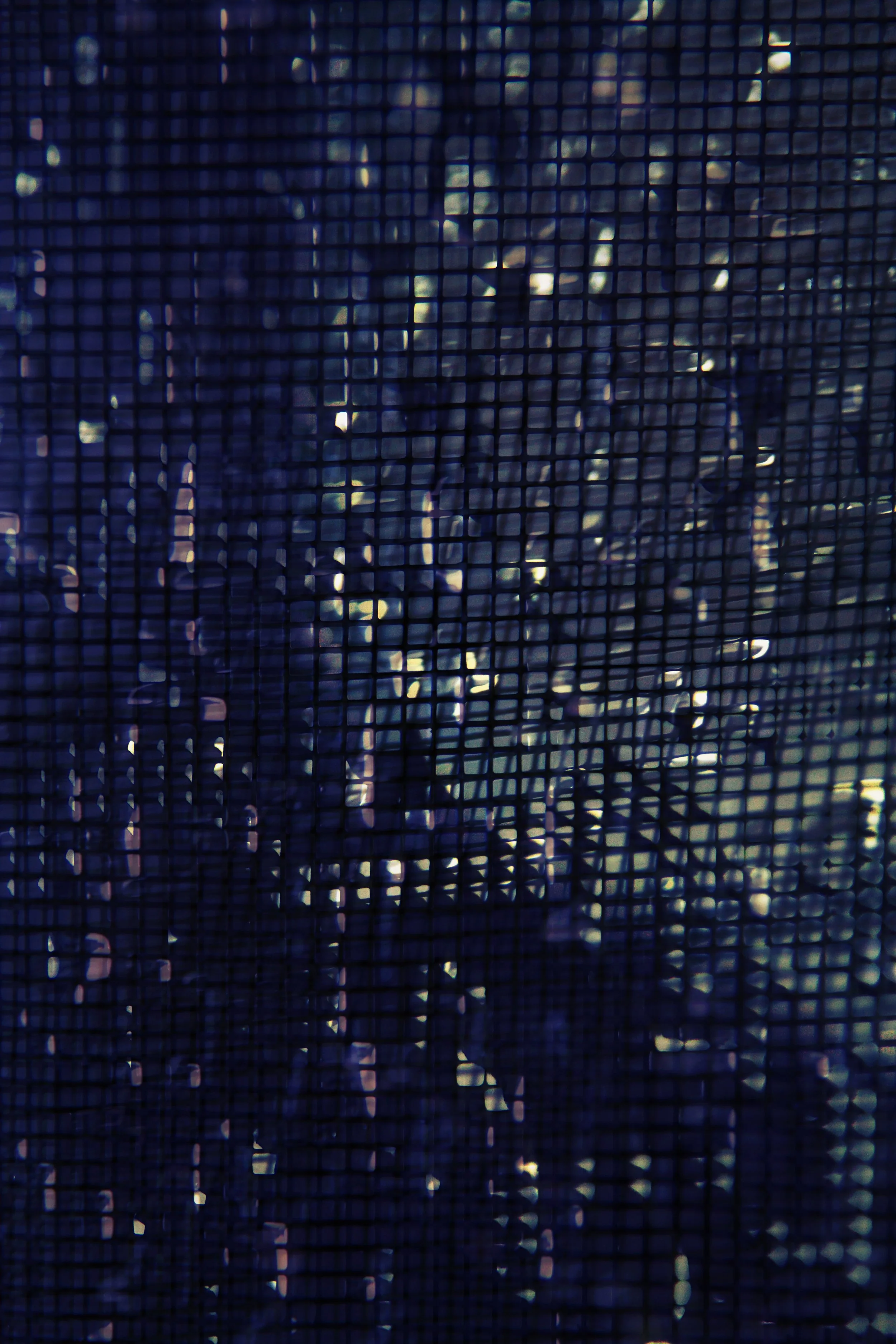 Silhouette of a person behind a dark grid or screen with small squares, with light shining through in the background.