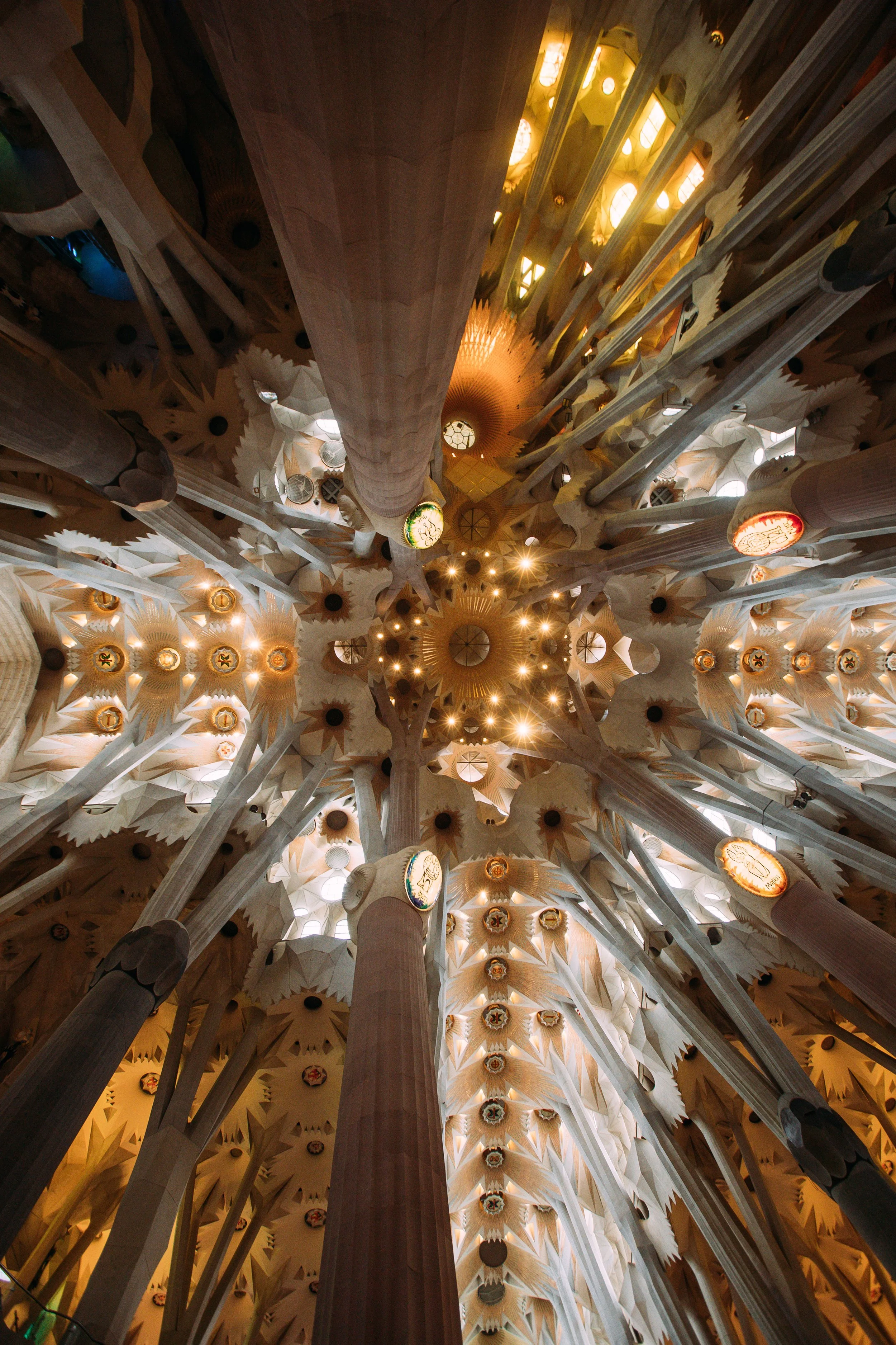 Interior view of the ceiling in the Sagrada Familia, showing tall columns and intricate, colorful, geometric patterns and designs.