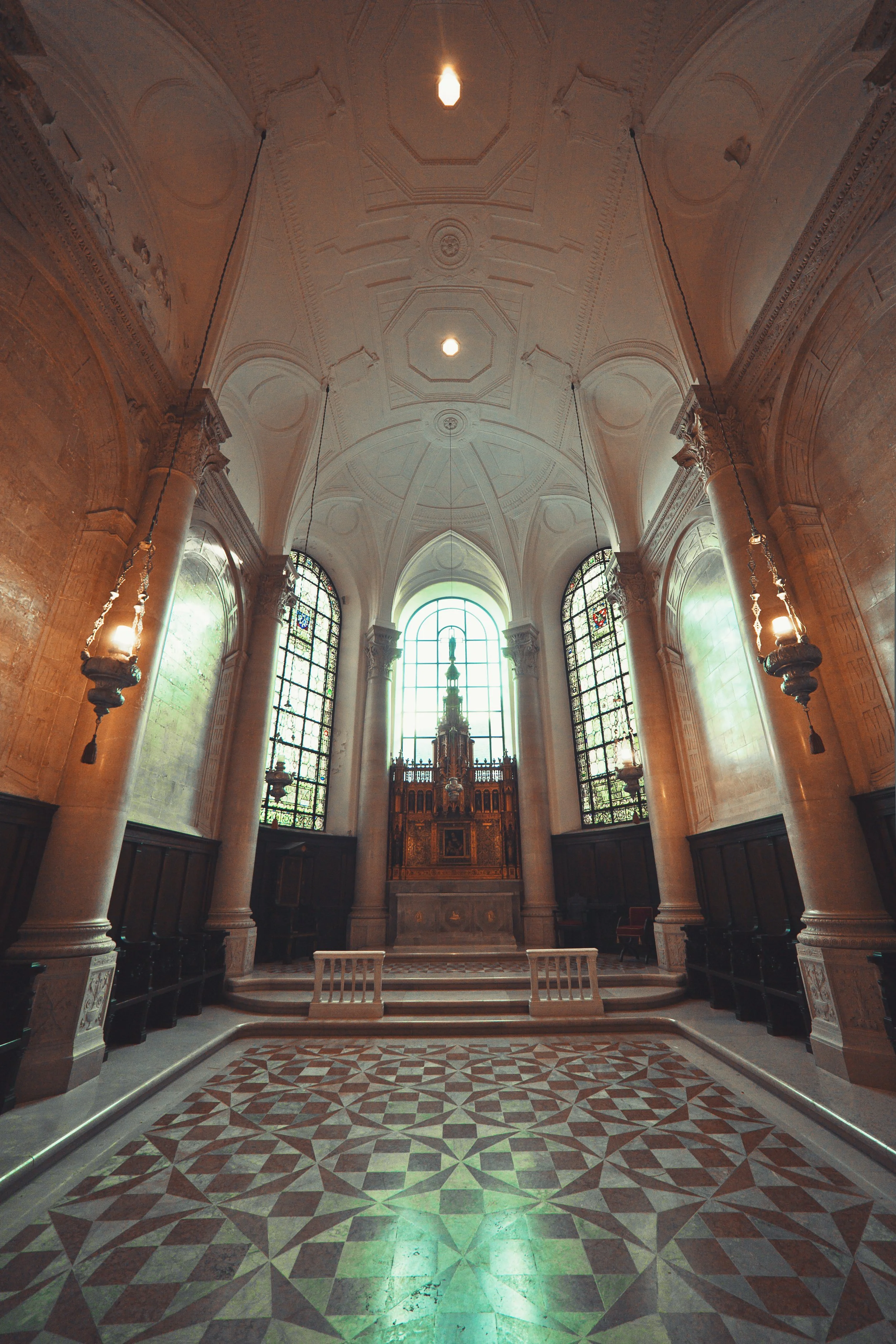 Interior of a historic church with high ornate ceiling, stained glass windows, altar at the back, stone columns, and patterned tile floor.