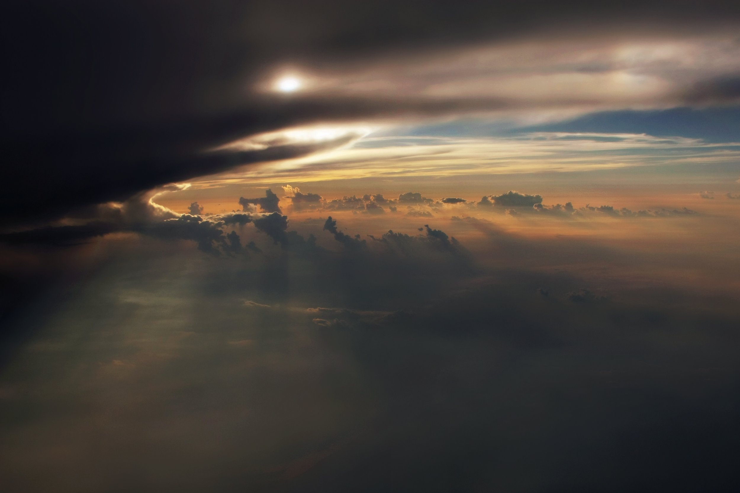 A sunset view through dark clouds with warm hues and streaks of light in the sky.