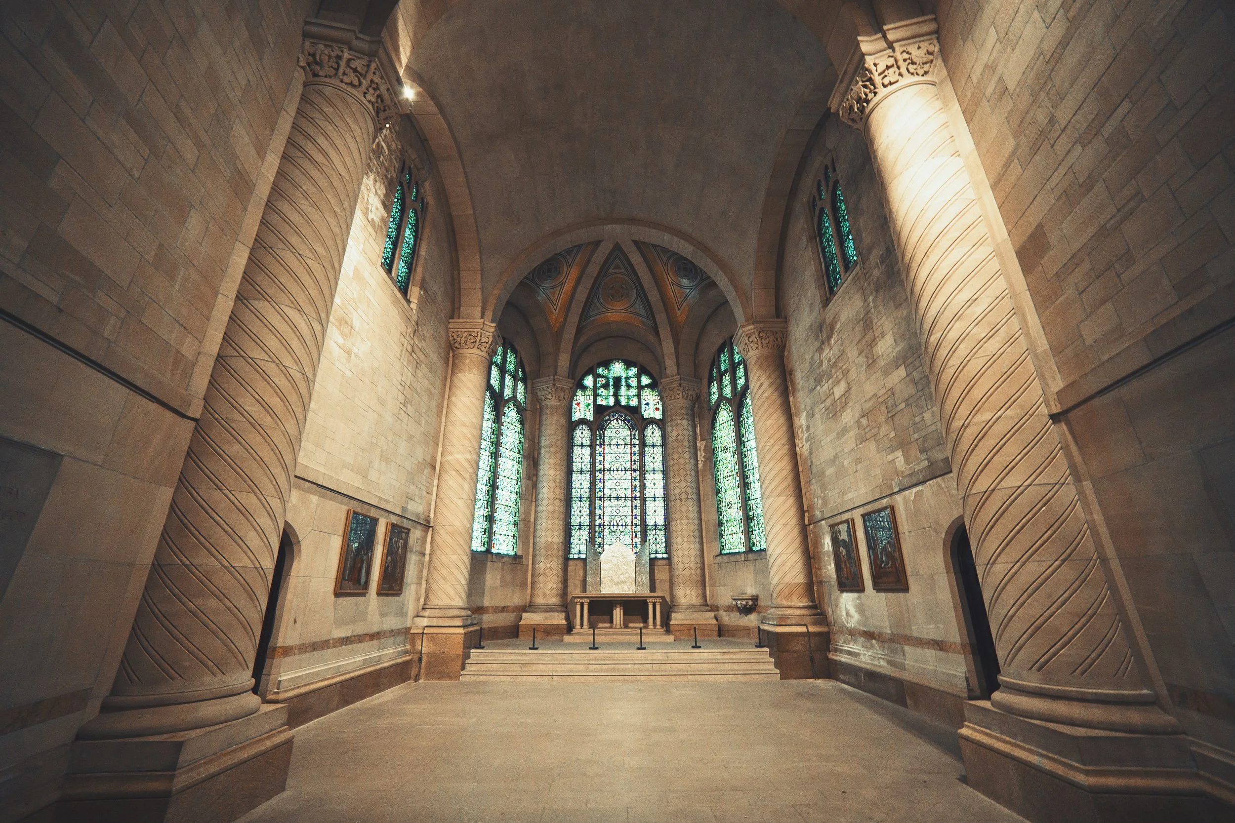 Interior view of a church with tall stone columns, stained glass windows, and a high vaulted ceiling.