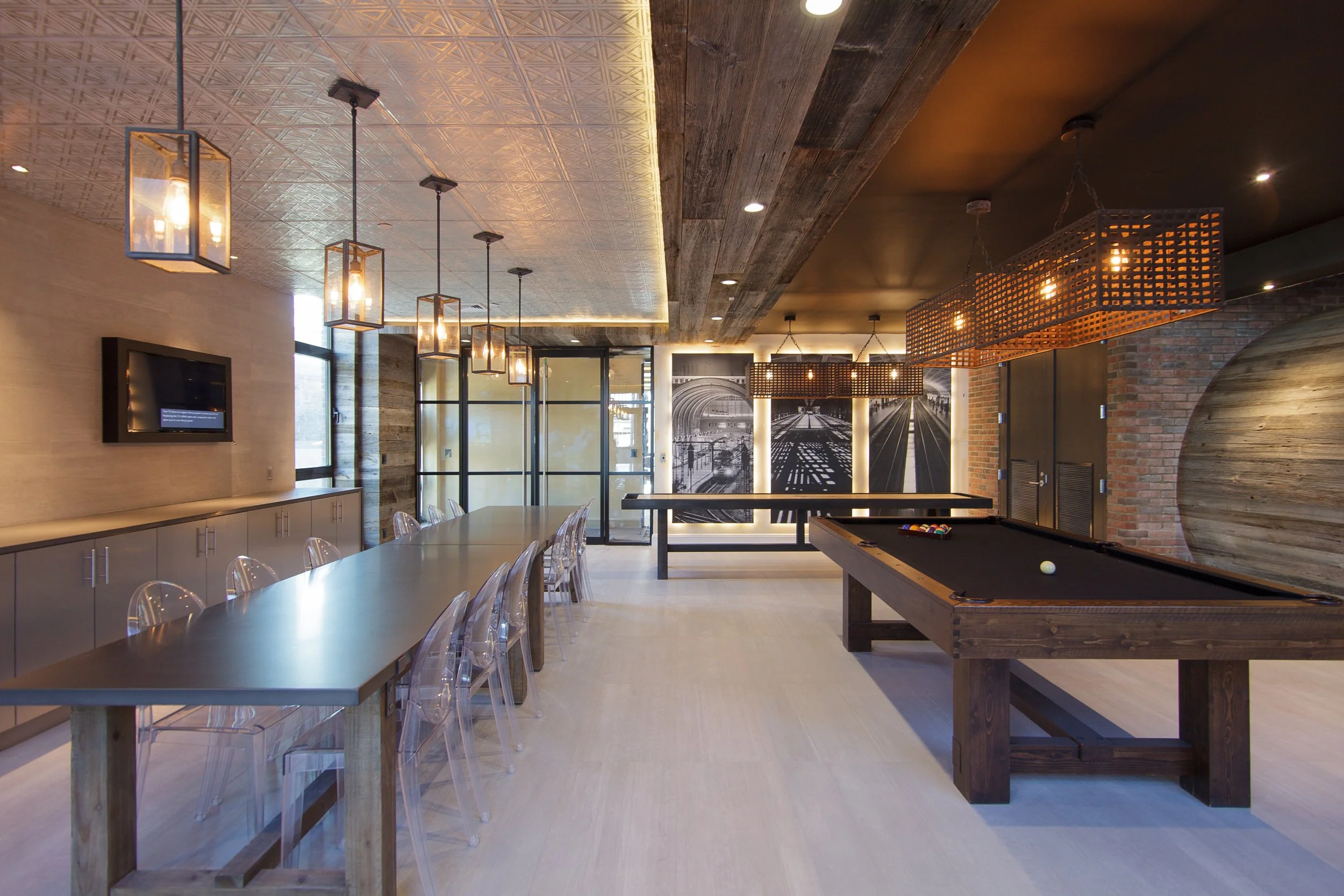 Modern interior of a recreational room with a long table and chairs, a pool table, decorative lighting, and black-and-white mural art.