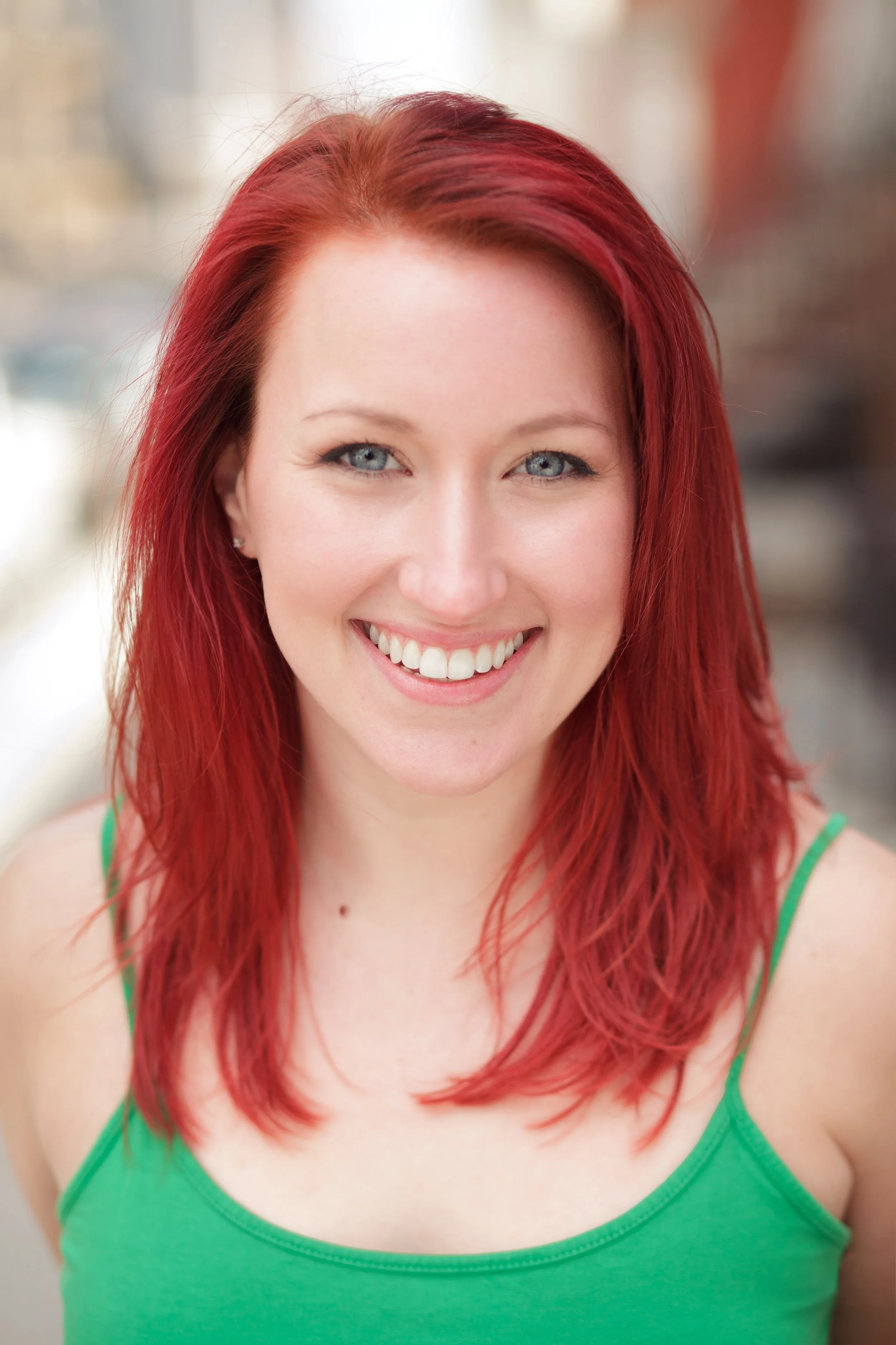 A woman with red hair and blue eyes smiling, wearing a green tank top.