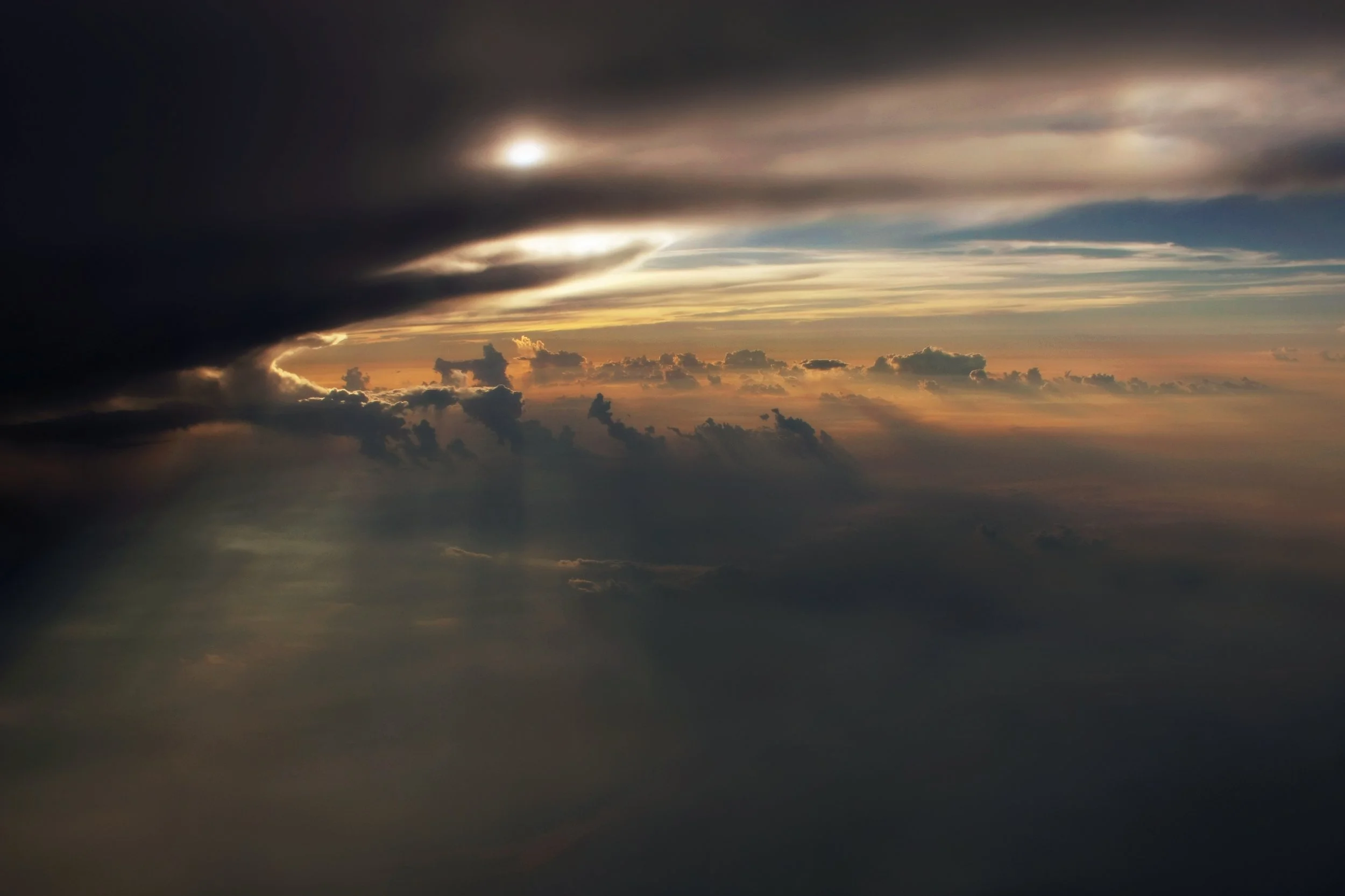 Sun partially obscured by dark clouds during sunset or sunrise with colorful sky and scattered clouds.