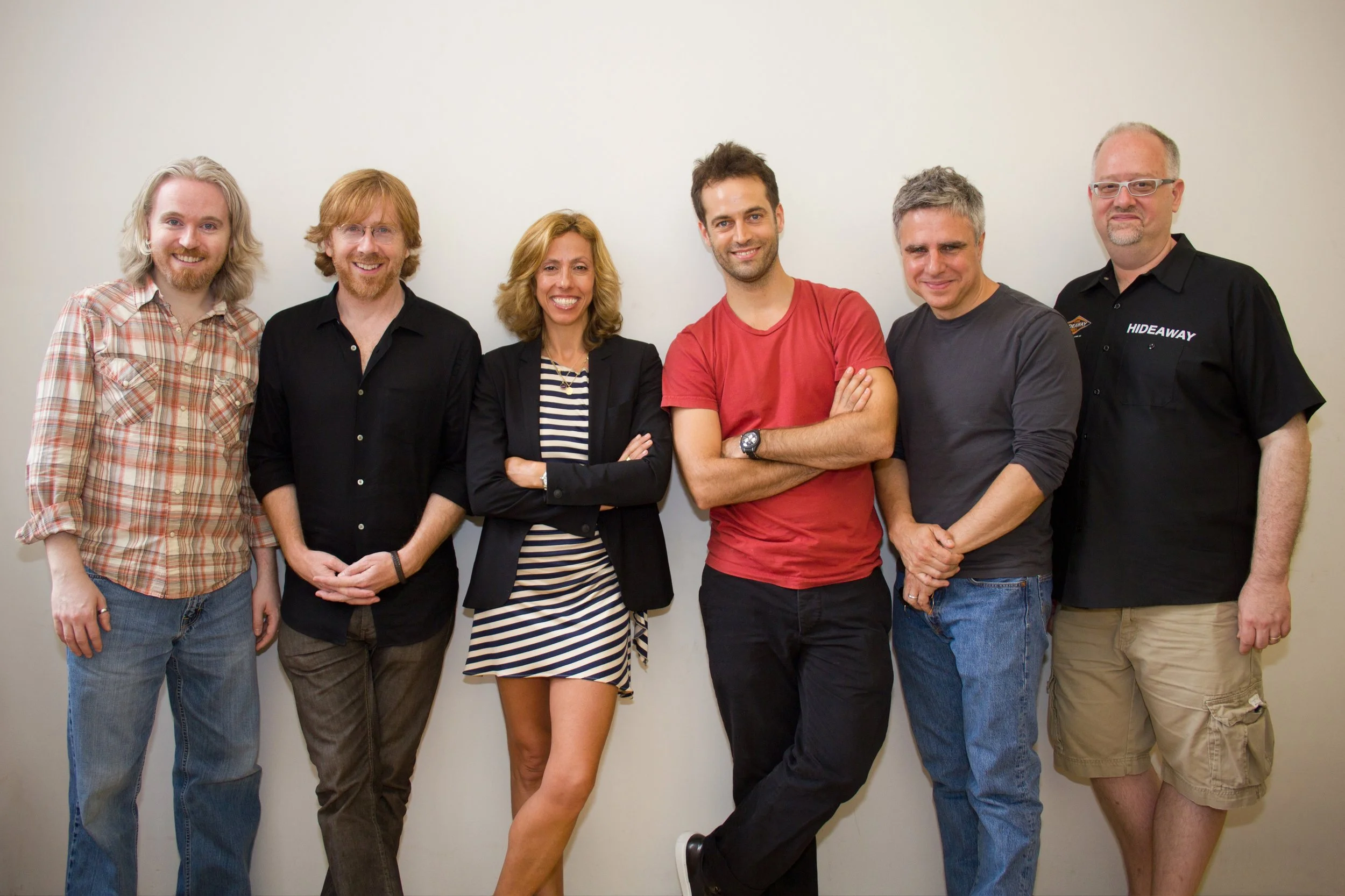 Group of six diverse smiling people standing against a plain wall.