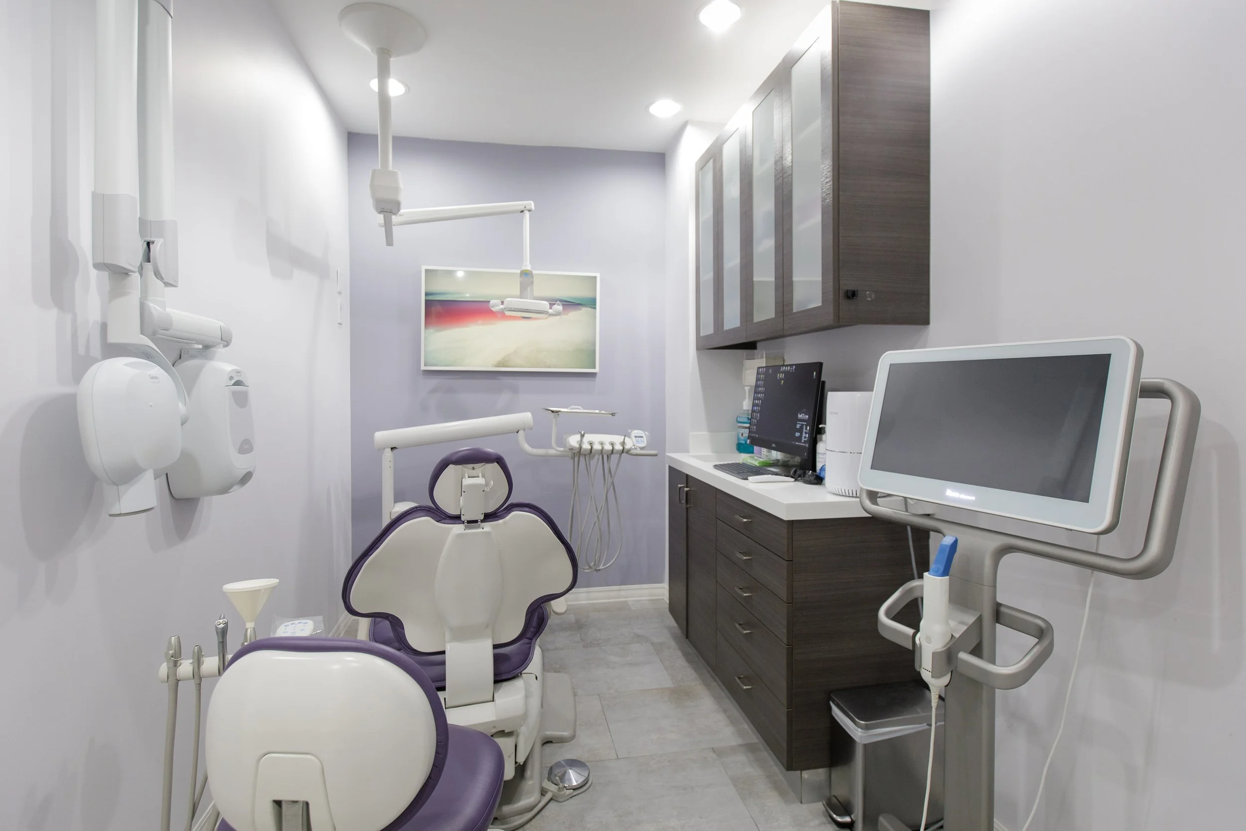 Dental examination room containing dental chairs, equipment, a computer, and cabinets.