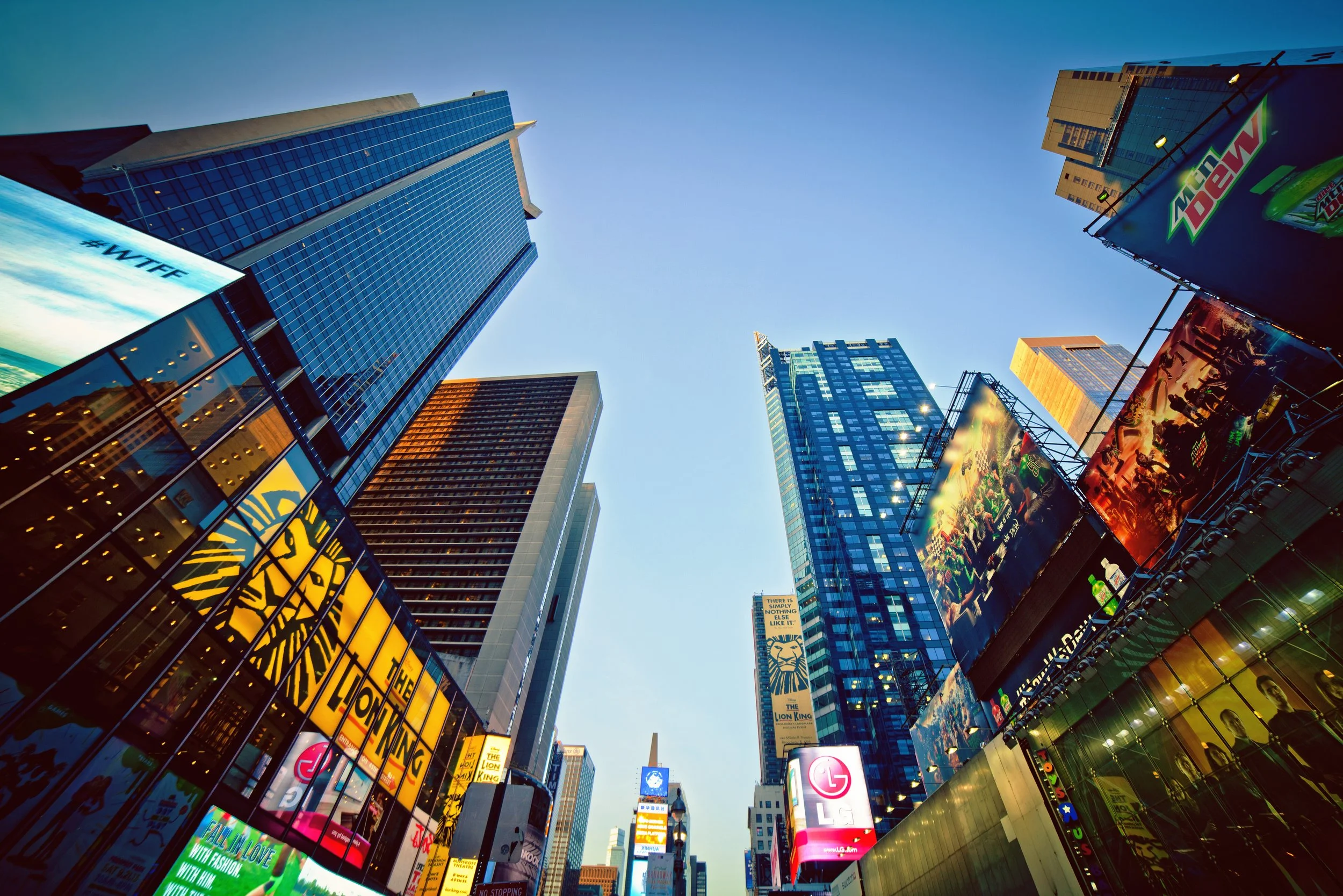 Cityscape of Times Square in New York City with tall buildings, digital billboards, and neon signs during the day.