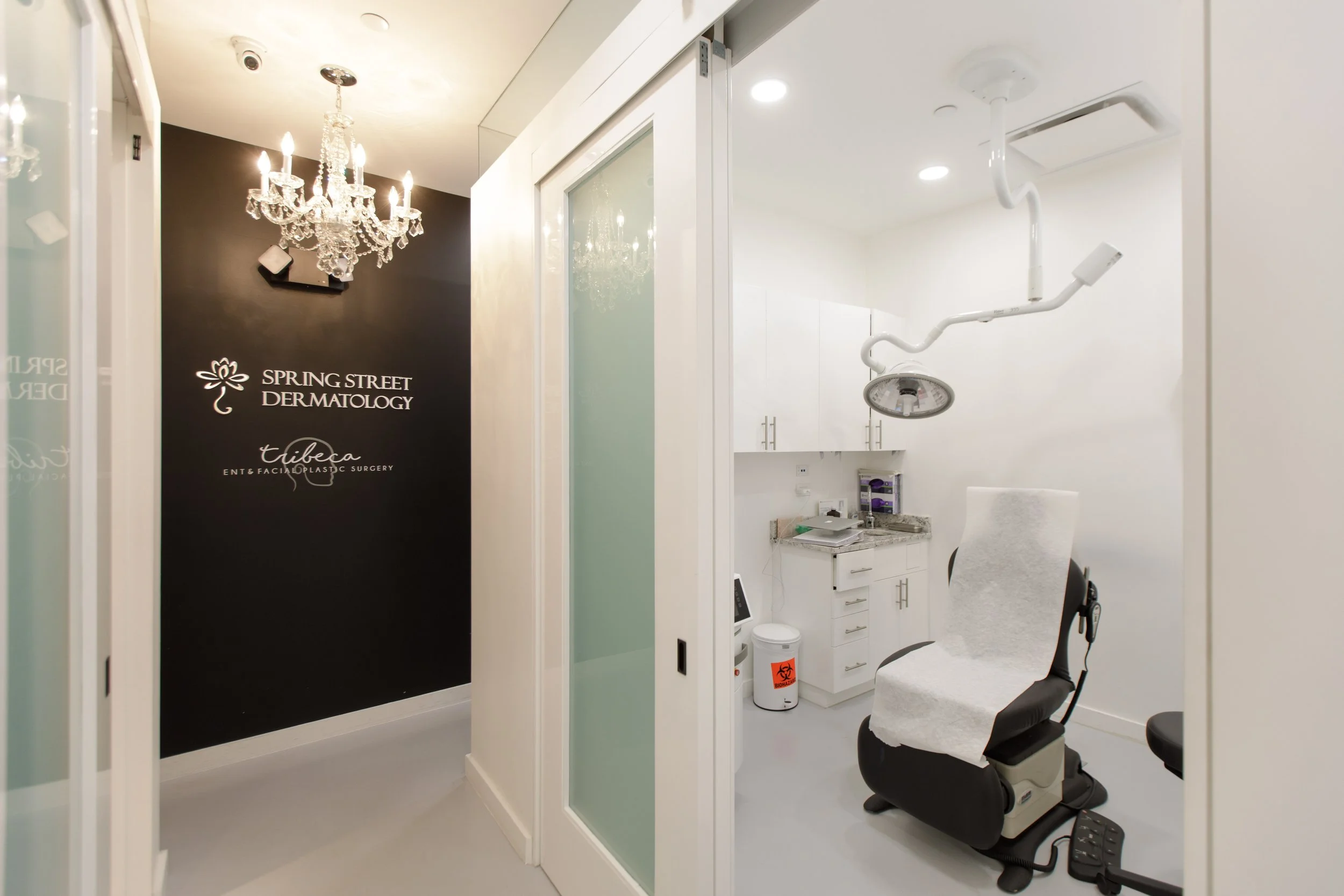Interior view of a medical or dental office with a chandelier, frosted glass sliding door, and a treatment area with dental chair, dental equipment, and cabinets.
