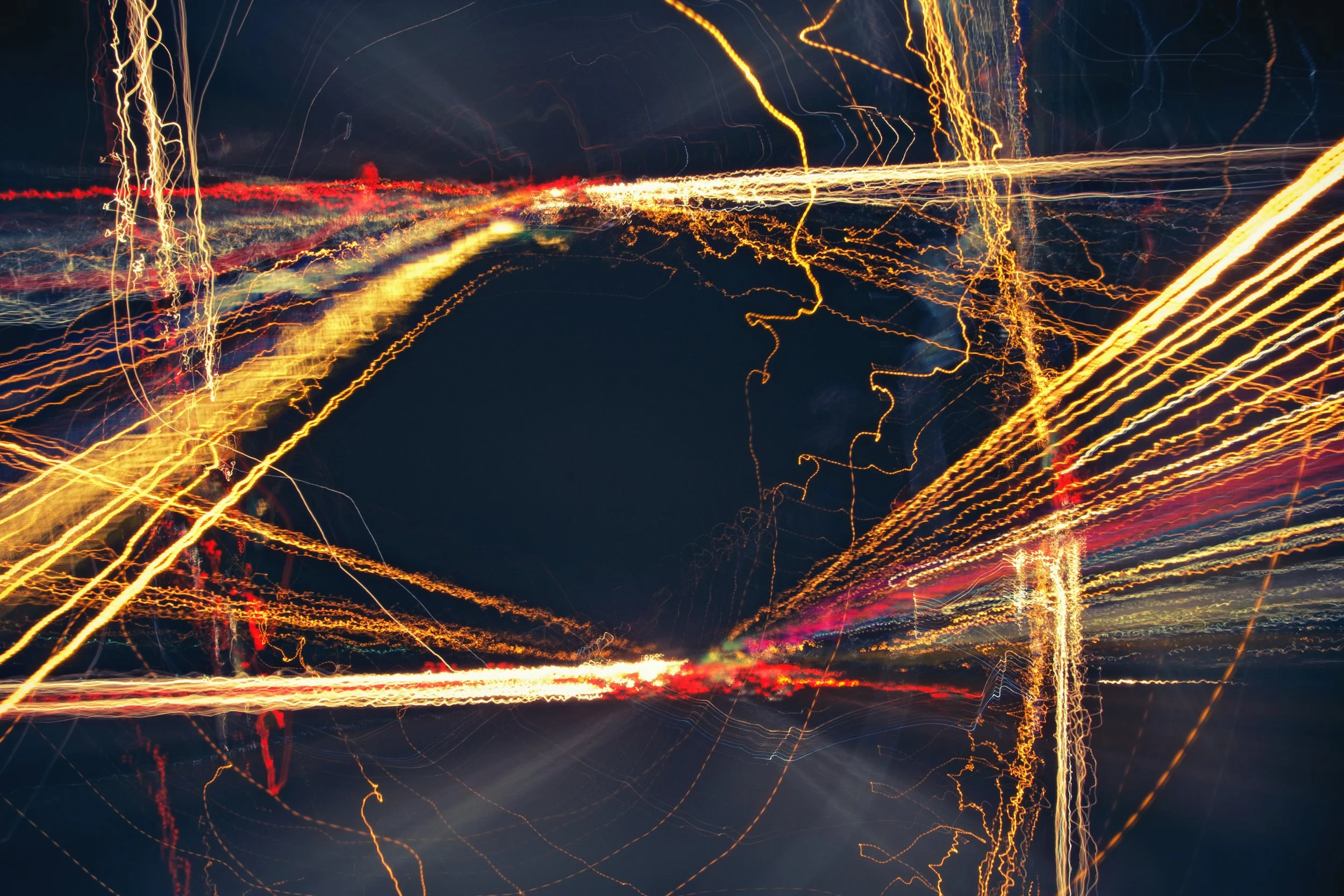 Long exposure of city lights at night, creating streaks and trails of yellow, red, and white light against a dark sky.