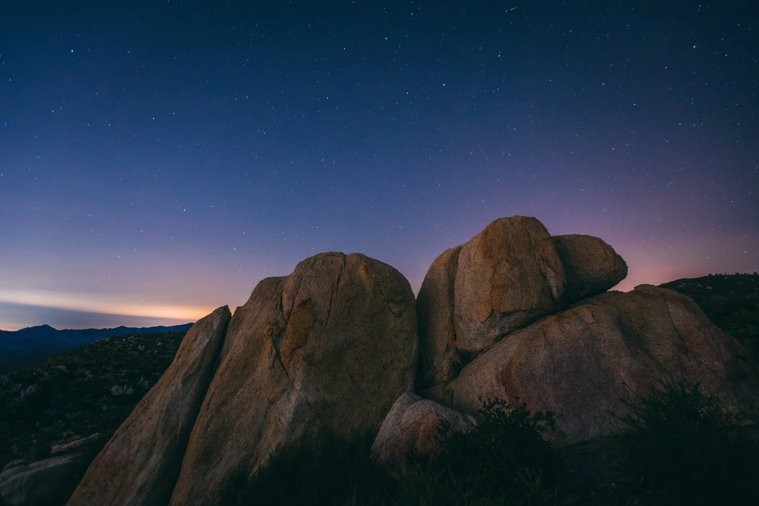 Nighttime landscape with large rocks in foreground and a starry sky above.