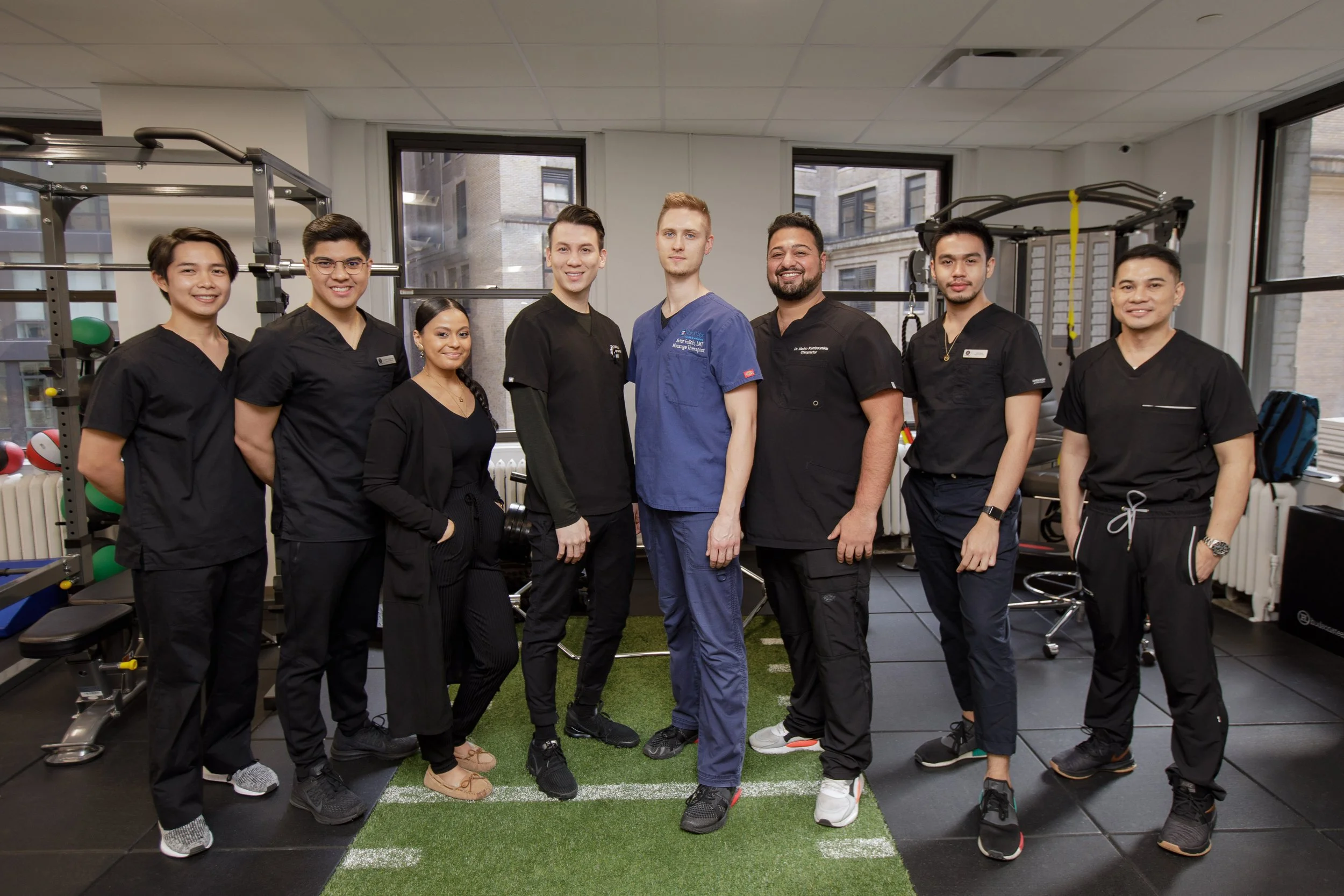 Group of diverse fitness professionals standing together inside gym with workout equipment and windows.
