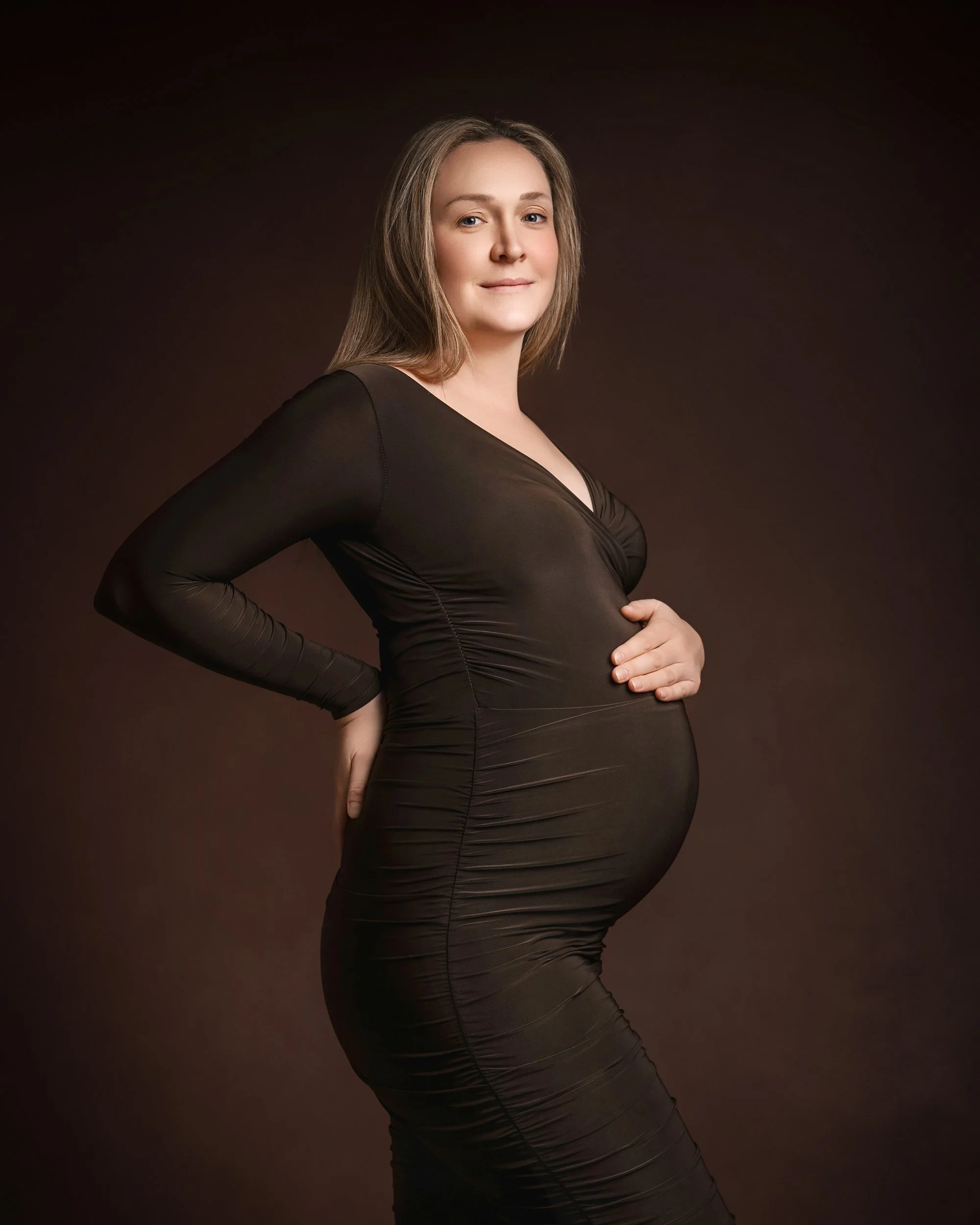 pregnant lady in tight brown dress holding belly photographed at kath evans photography studio talgarth brecon mid wales
