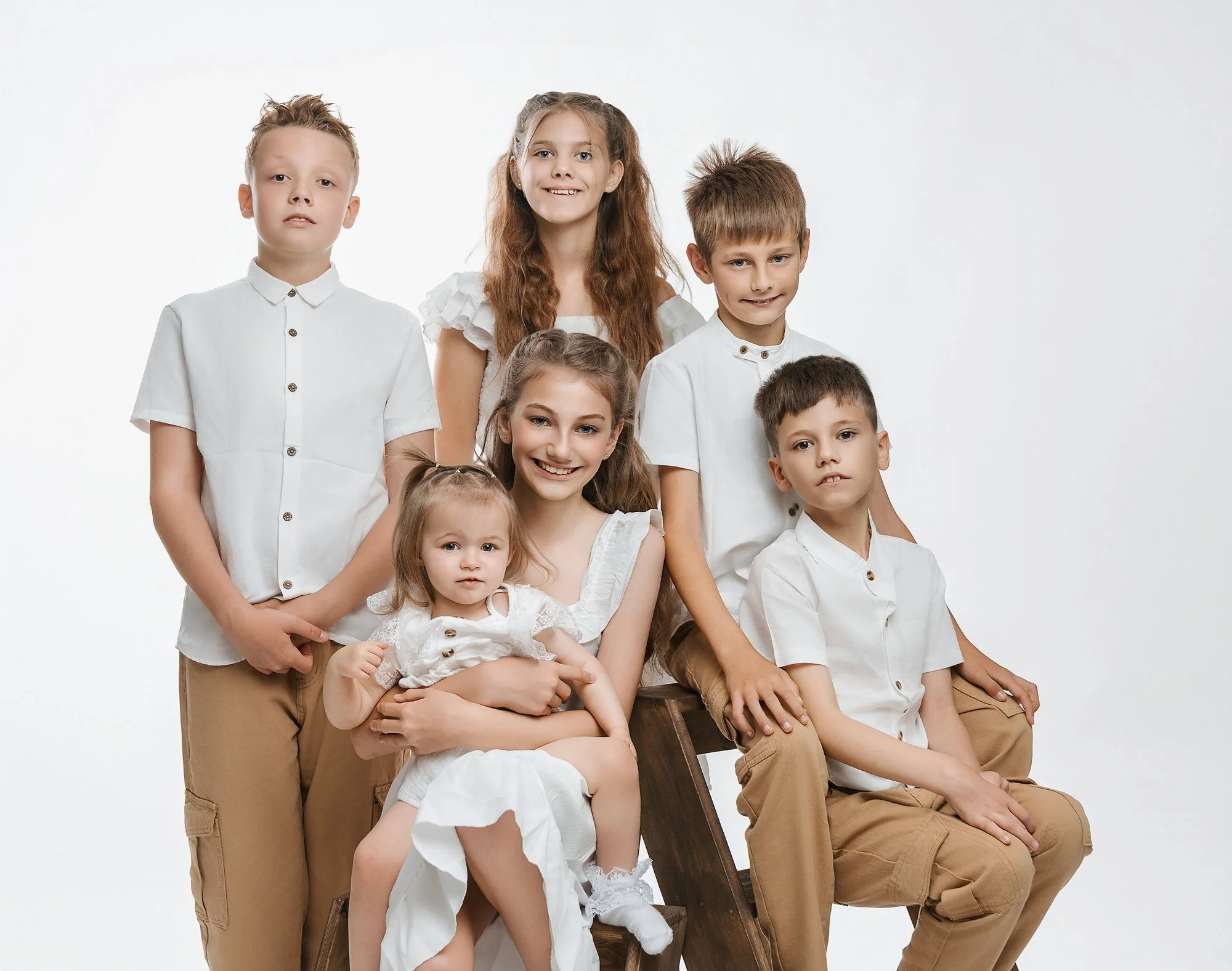 Group of seven children dressed in white shirts and beige pants, posed against a plain white background. photographed at kath evans photography studio talgarth brecon mid wales