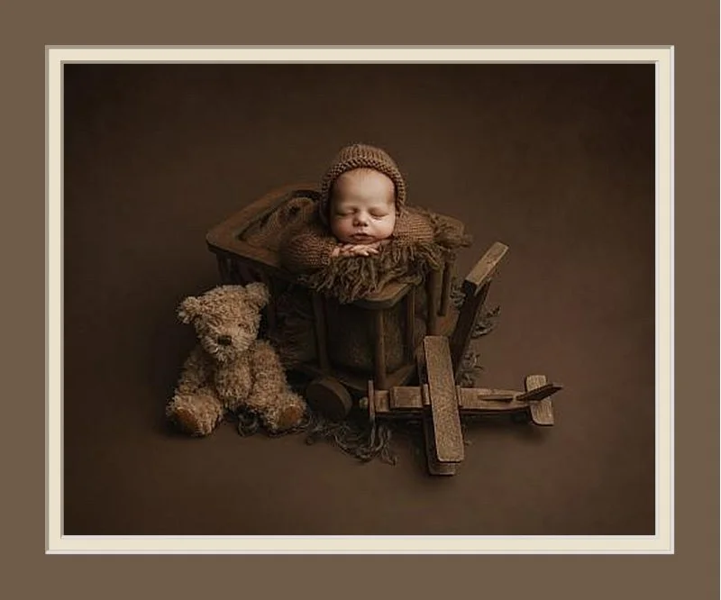 Sleeping baby wearing a knitted bonnet, holding a small knitted teddy bear, on a beige surface.