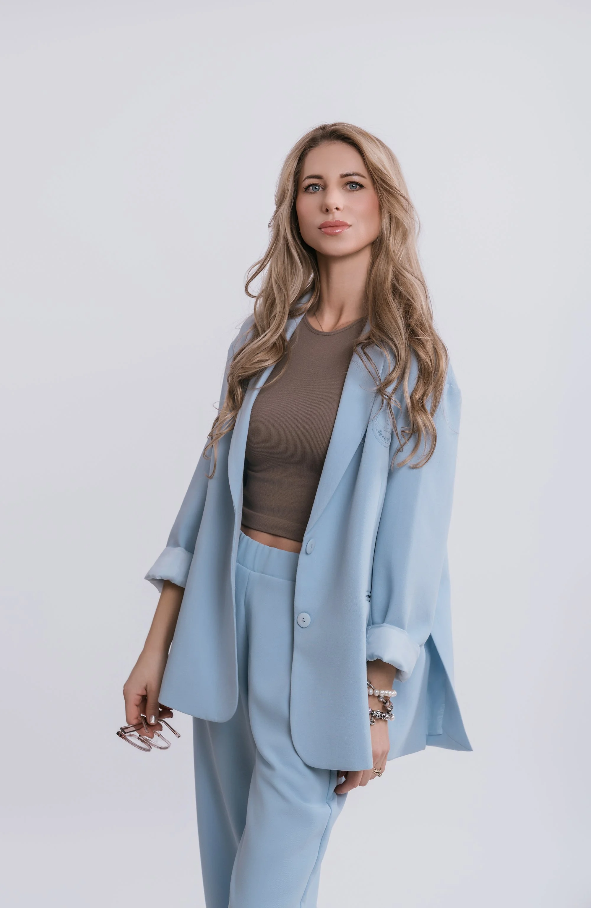 A woman with long blonde hair smiling, sitting at a wooden desk with an HP computer monitor and keyboard, in a modern office setting.
