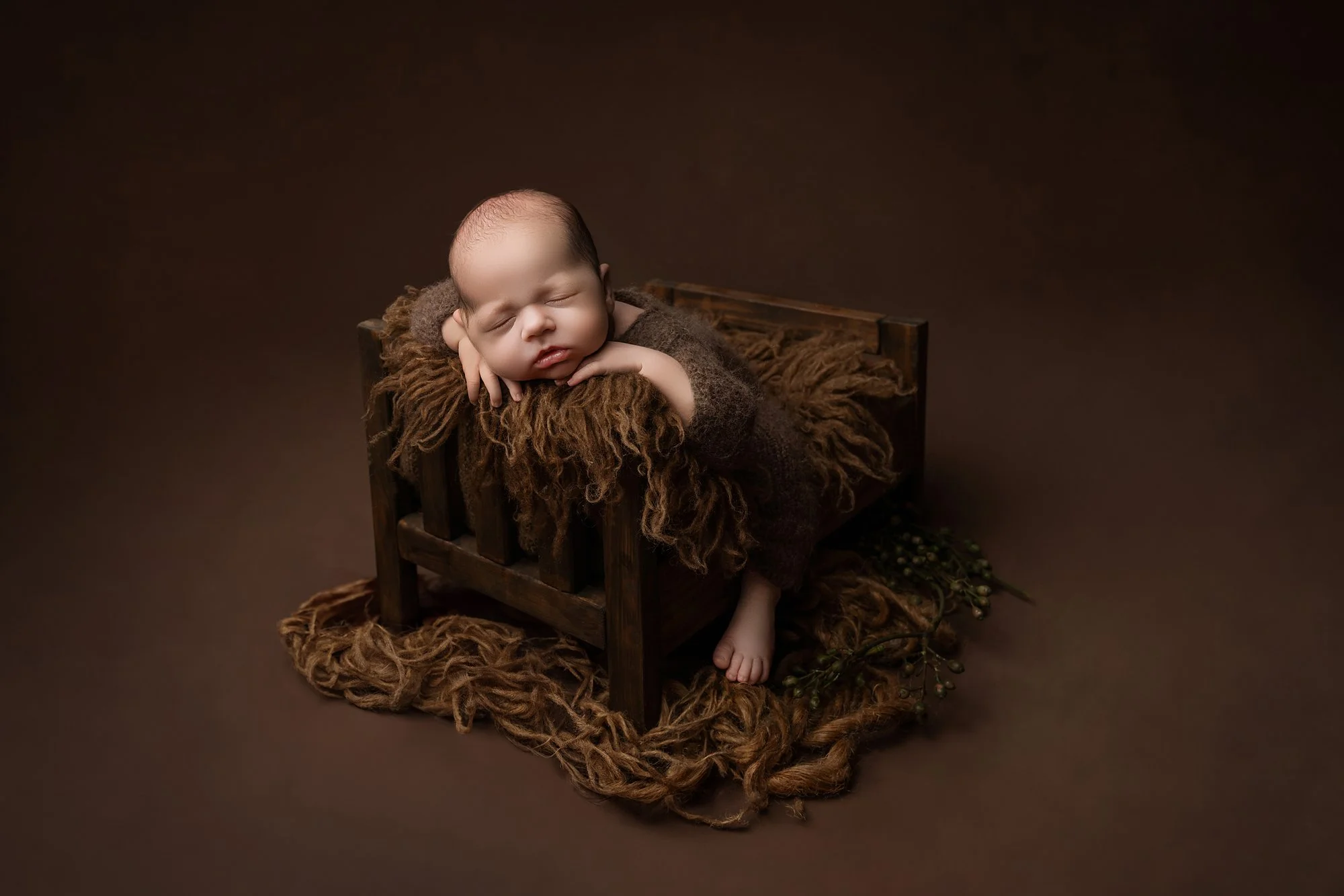 a sleeping newborn on a tiny newborn bed on a brown backdrop photographed at kath evans photography studio talgarth brecon mid wales