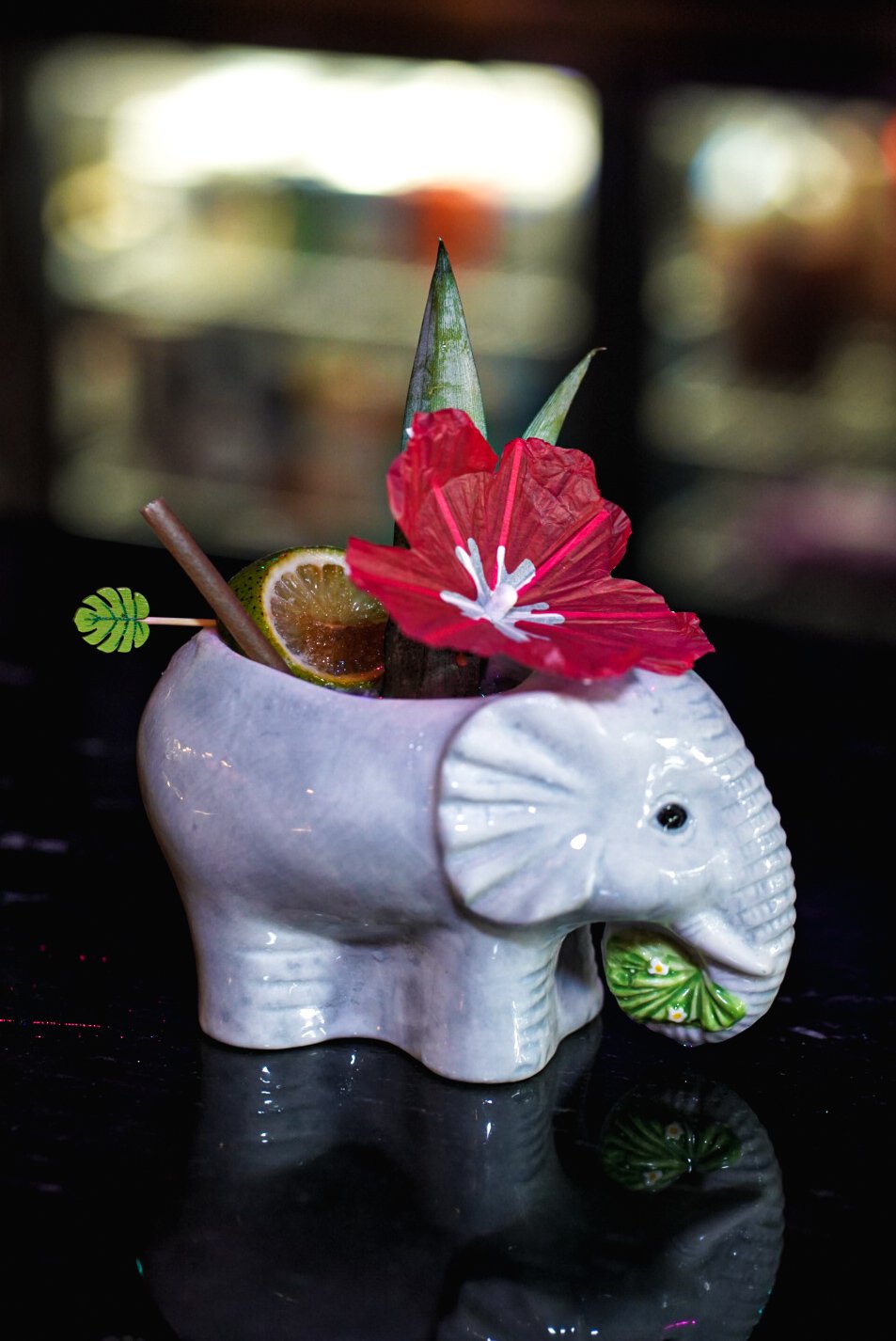 A ceramic elephant-shaped container holding a tropical drink garnished with a red hibiscus flower, lime slices, and a small decorative leaf.