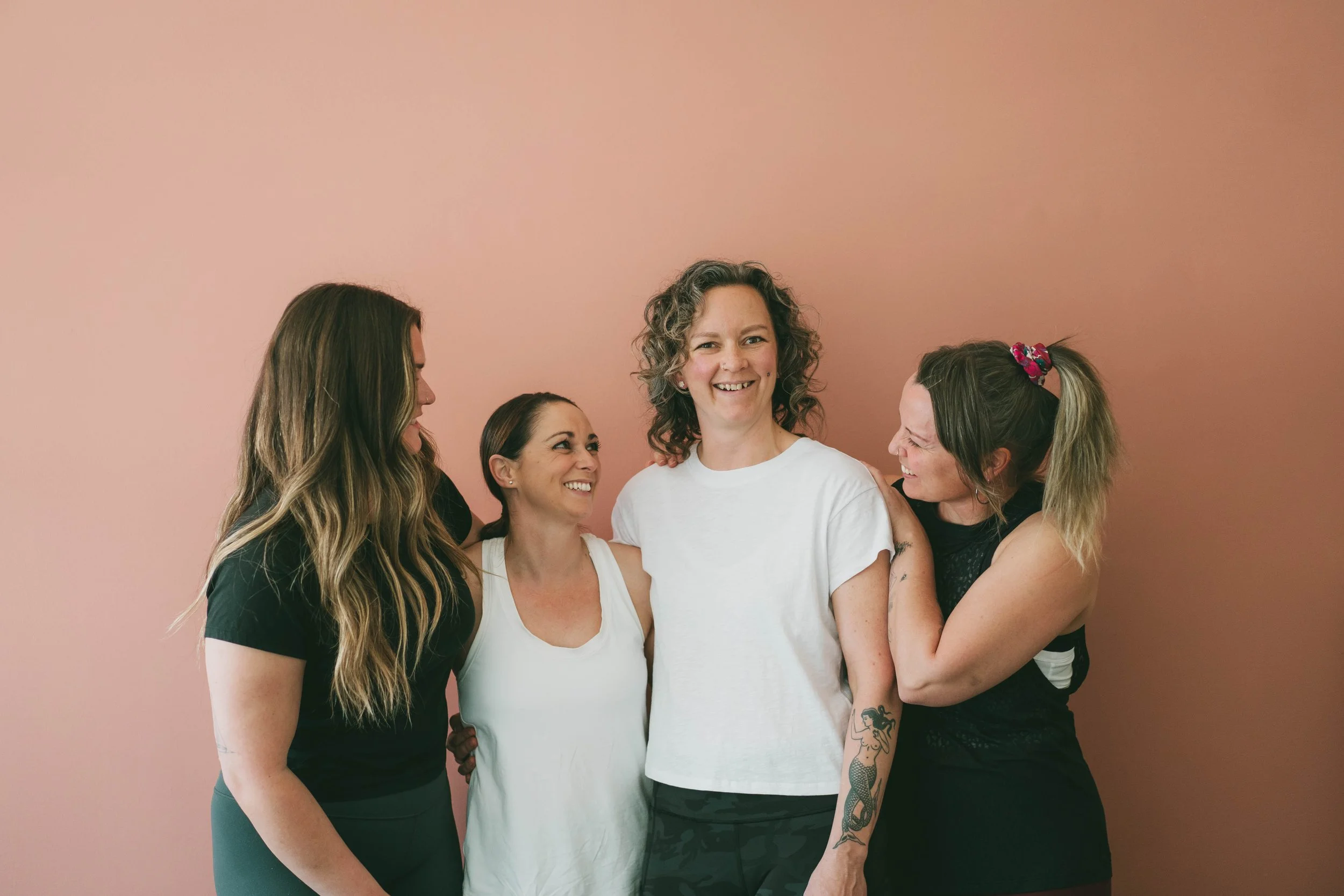 Five instructors standing together in front of a pink wall, smiling and laughing.
