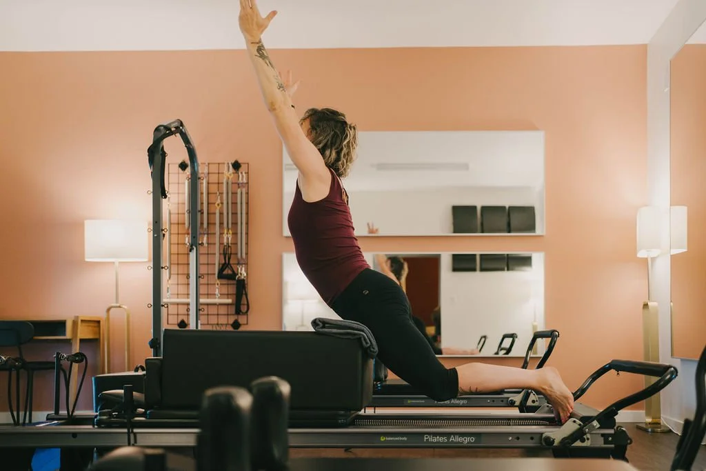 People participating in a Pilates class in a studio, using reformer machines, led by an instructor.