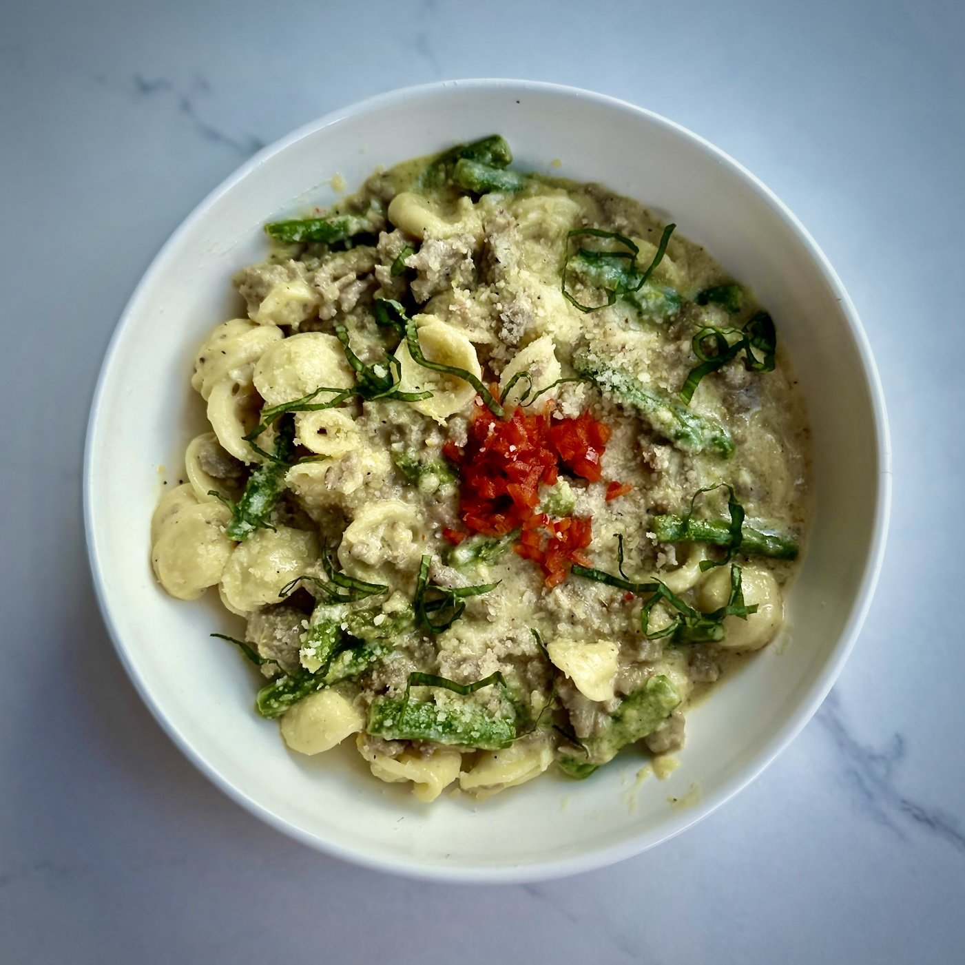 Pasta dish with orecchiette, asparagus, ground meat, red bell pepper, and fresh herbs in a creamy sauce served in a white bowl. Baby shower, wedding shower, wedding, celebration, private dining, private events, birthdays, custom menu. restaurant rent