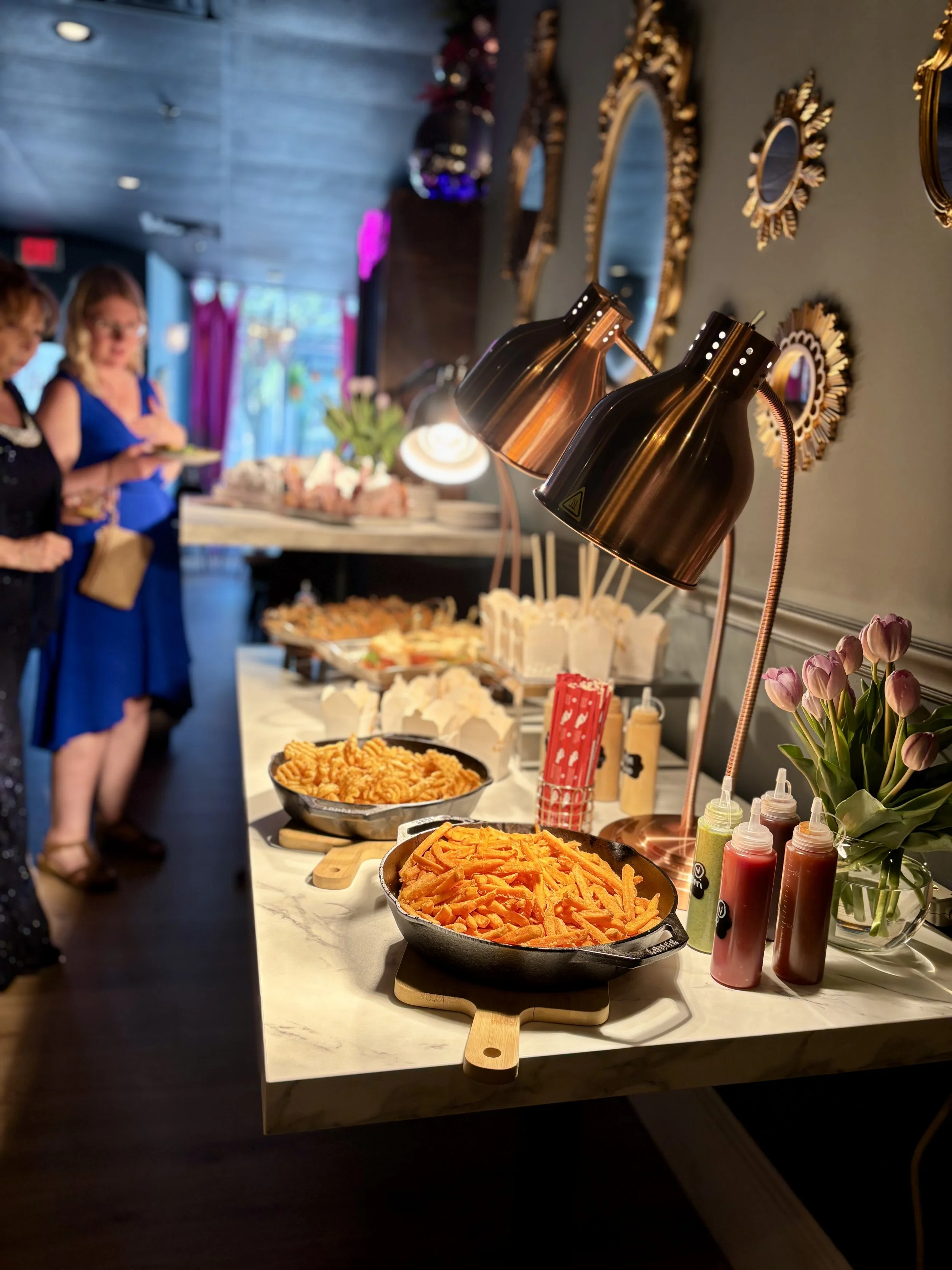 Buffet table with sweet potato fries, curly fries, condiments, and tulips on a white marble surface.Best Smash Burger Near Me Nashua NH Burgers Best of Nashua