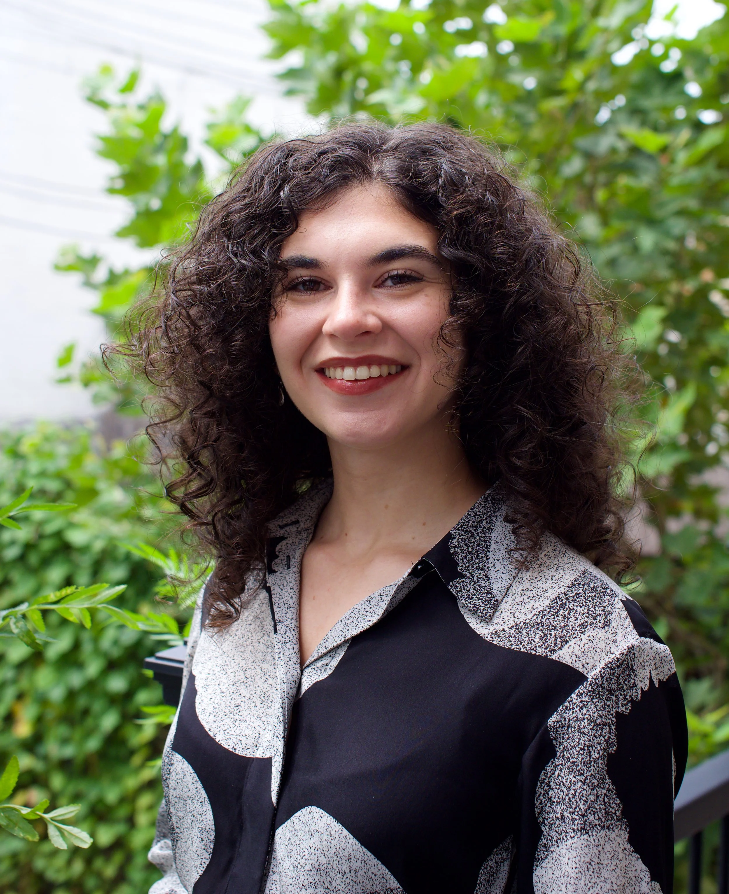 Emma, a white Latina woman with big curly hair, smiles at the camera.