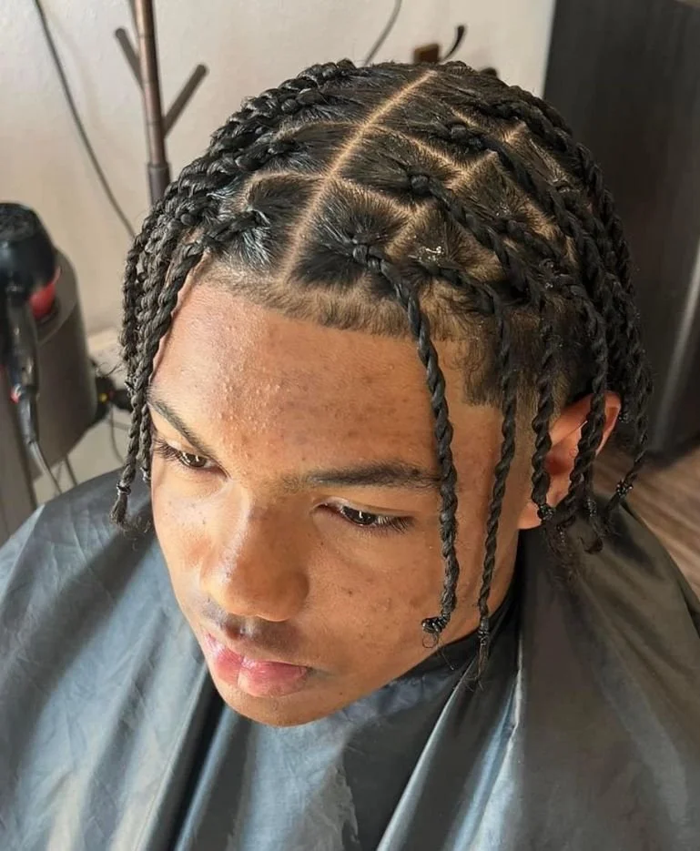 Young person with braided hairstyle at a salon, wearing a black cape.